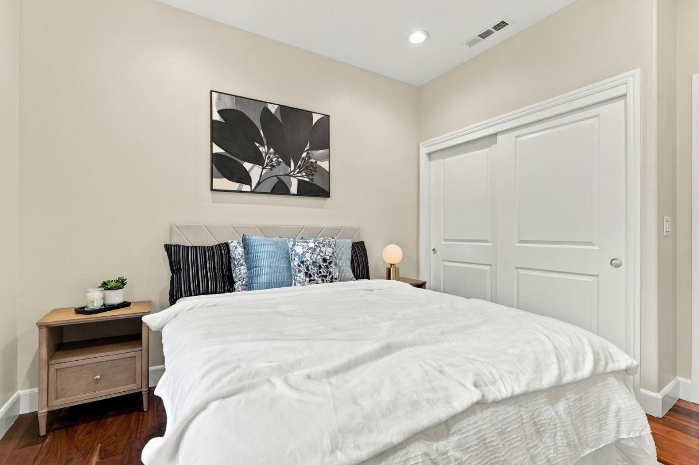 Staged bedroom with a white bed, blue accent pillows, botanical wall art, and sliding closet doors.