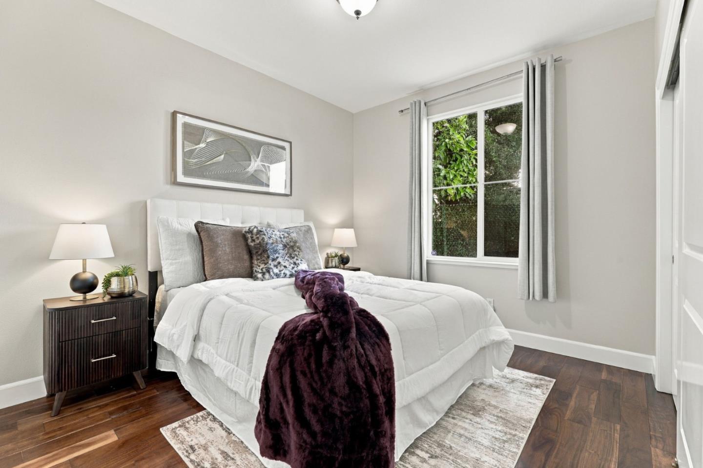 Staged bedroom with a white bed, purple throw, and window framed by gray curtains.
