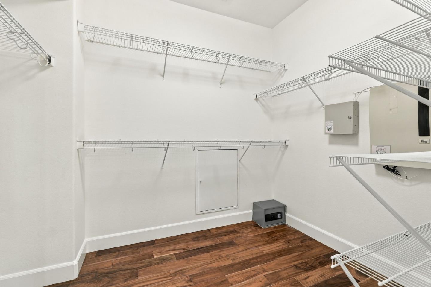 Walk-in closet with wire shelving, dark wood floors, and a small safe.