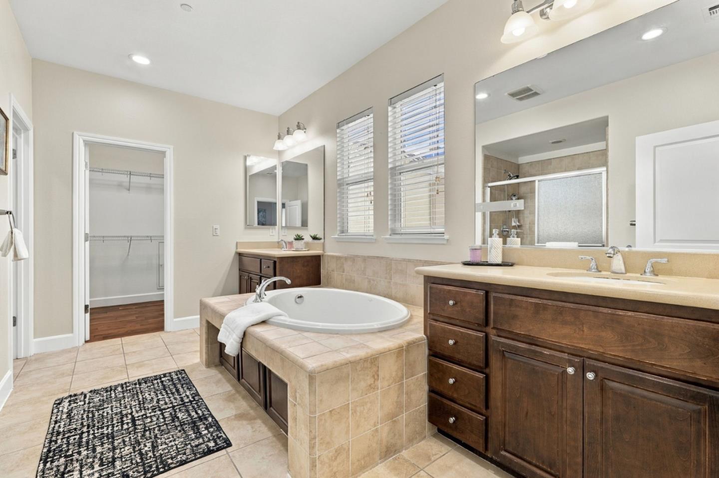 Primary bathroom with a tiled soaking tub, dark wood double vanity, and windows with blinds.