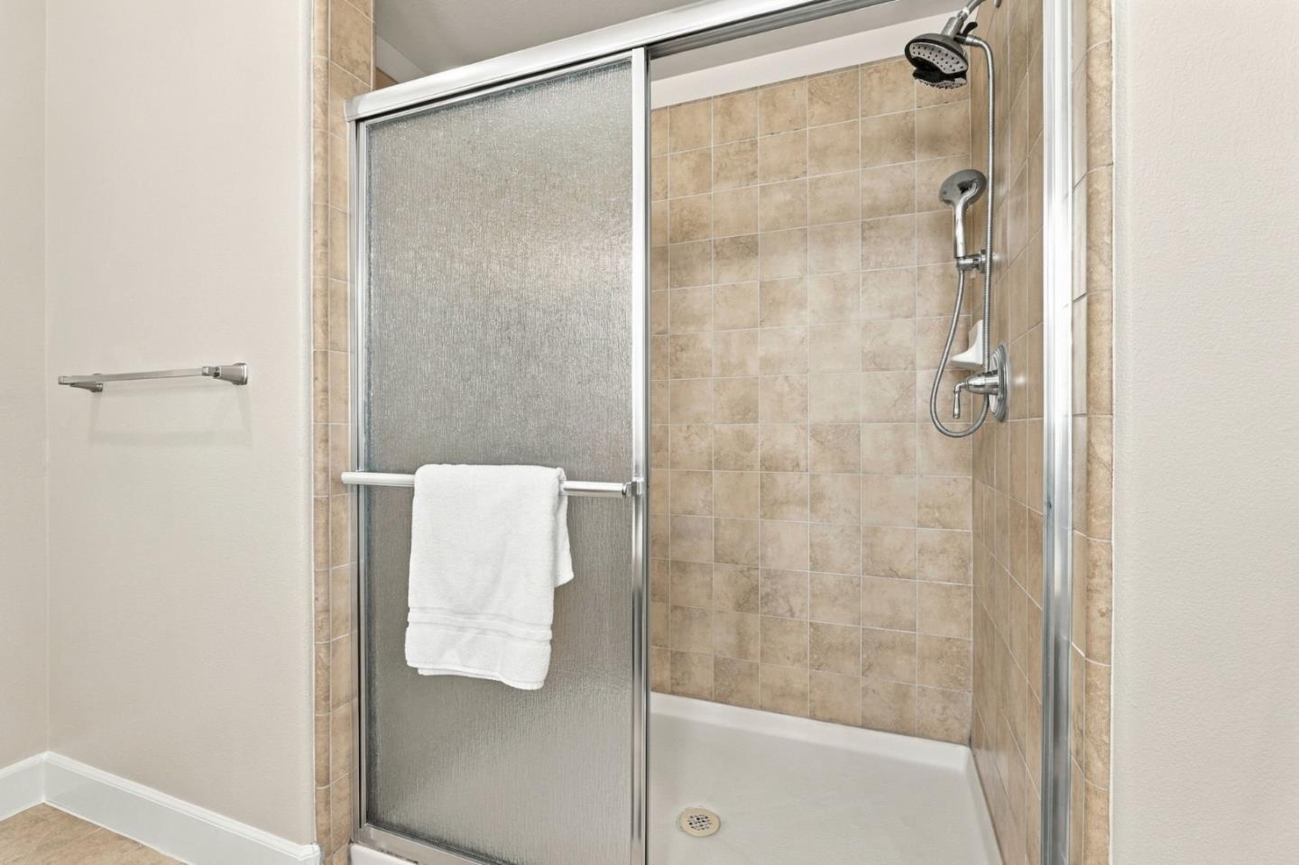 Bathroom shower with beige tile, a white tub, sliding glass door, and two showerheads.