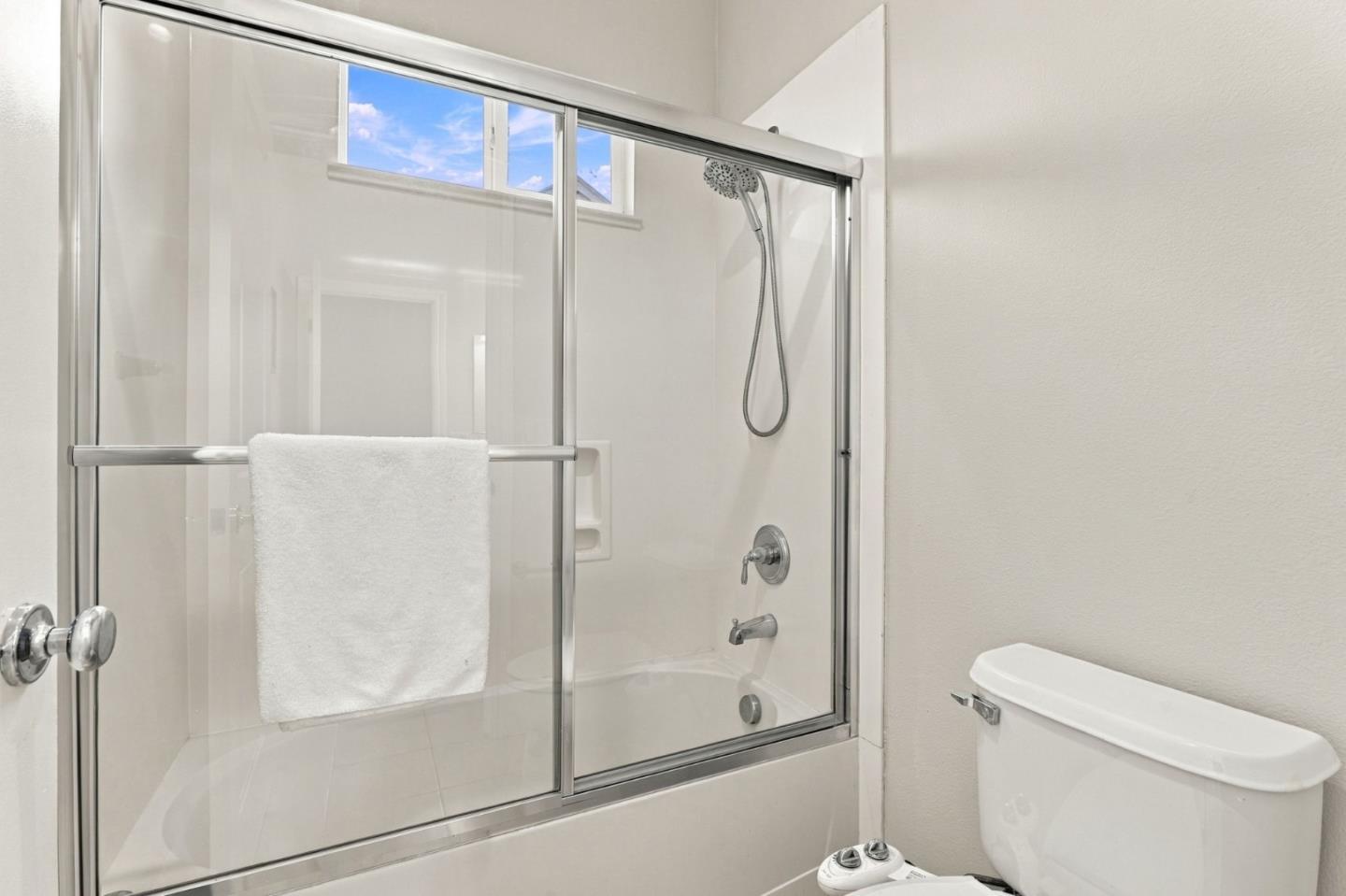 Bathroom tub and glass-enclosed shower with chrome fixtures and a towel on the door.