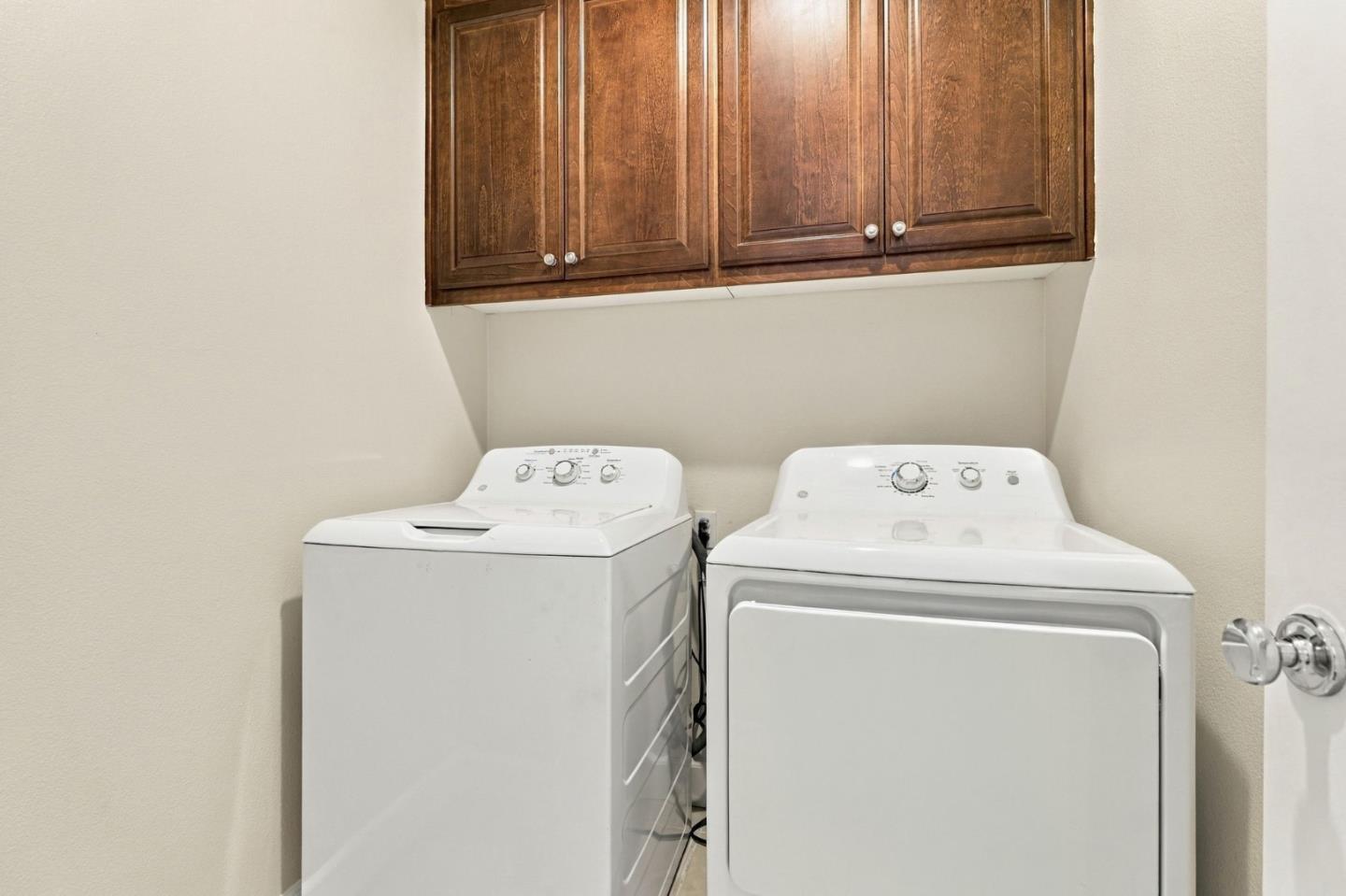 Laundry area with a white washer and dryer beneath dark wood cabinets.