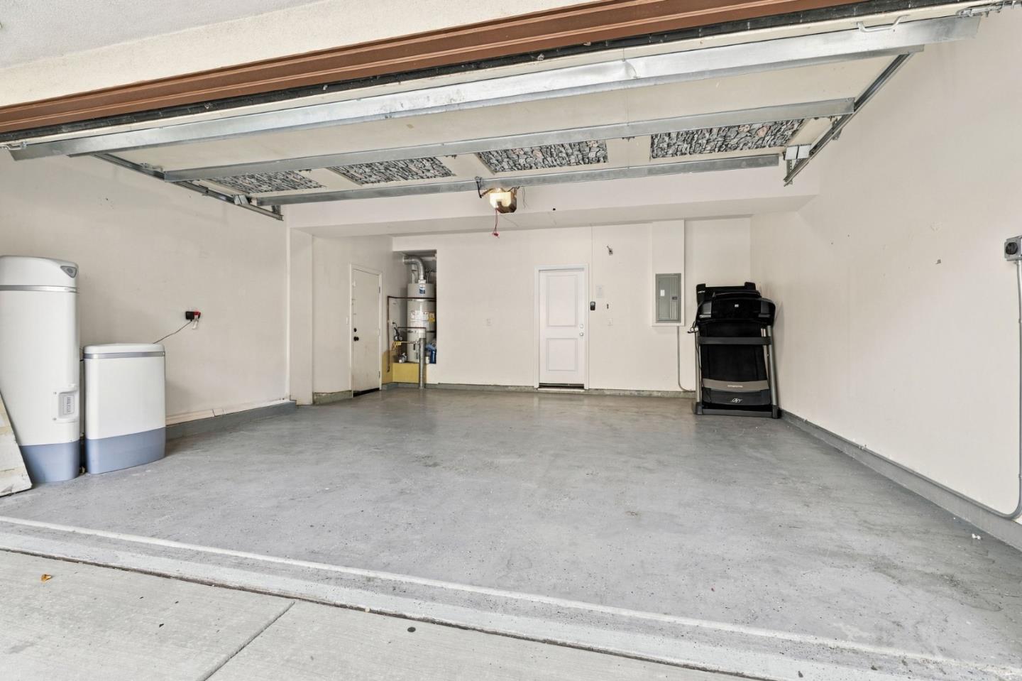 Mostly empty garage with an open overhead door, two water heaters, and a folded treadmill.