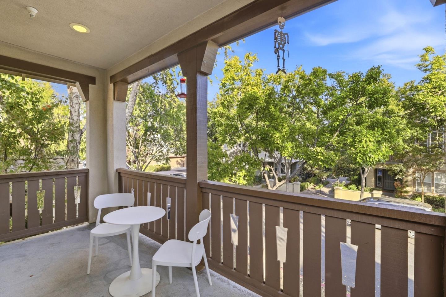 Covered balcony with white patio seating and leafy trees beyond the railing.