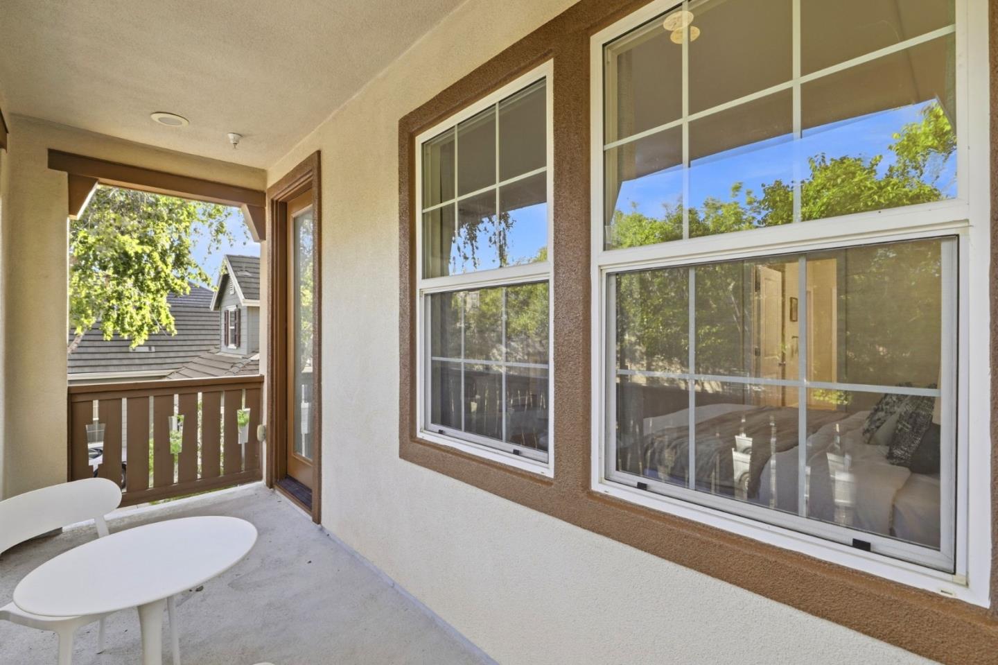 Covered balcony with a white table and chairs beside large windows.