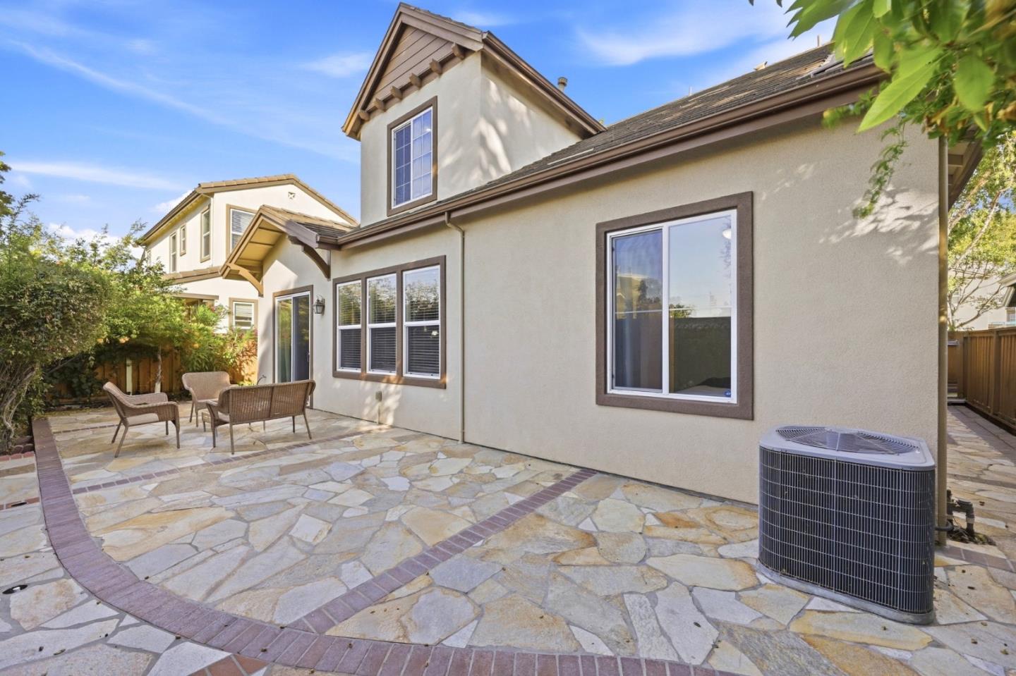Home’s rear patio with flagstone paving, outdoor chairs, and a two-story stucco exterior.