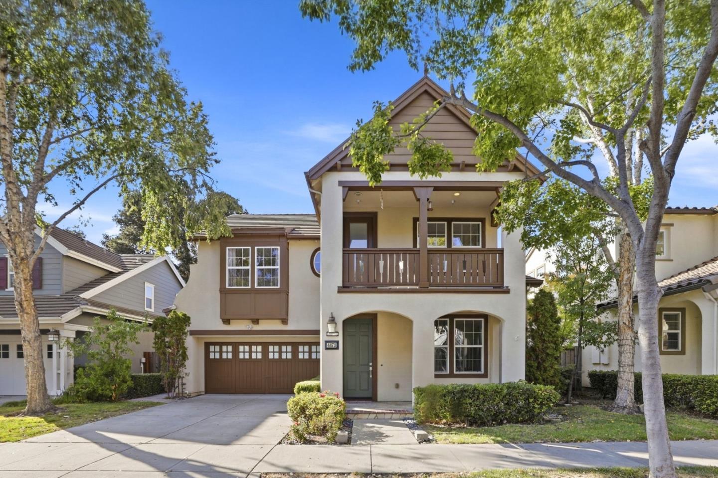 Two-story stucco home with a covered balcony, brown-trimmed garage, and mature trees.