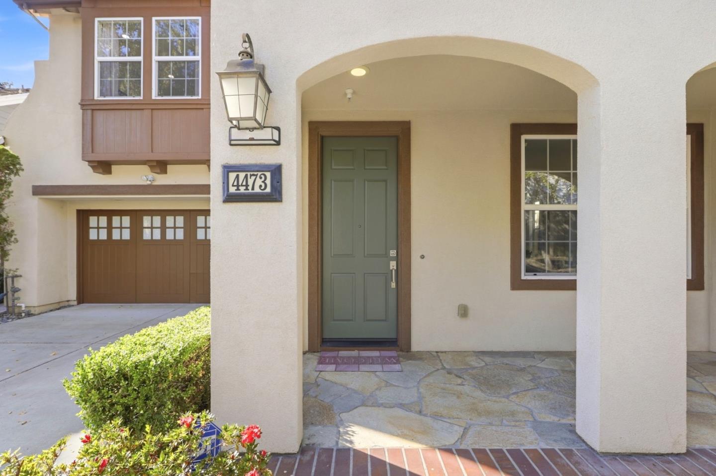 Home entrance with an arched porch, green door, stone paving, and attached garage.