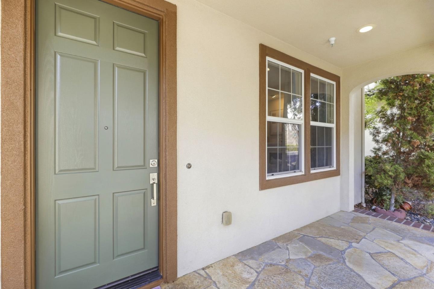 Entry porch with a sage-green front door, brown-trimmed windows, and stone paving.