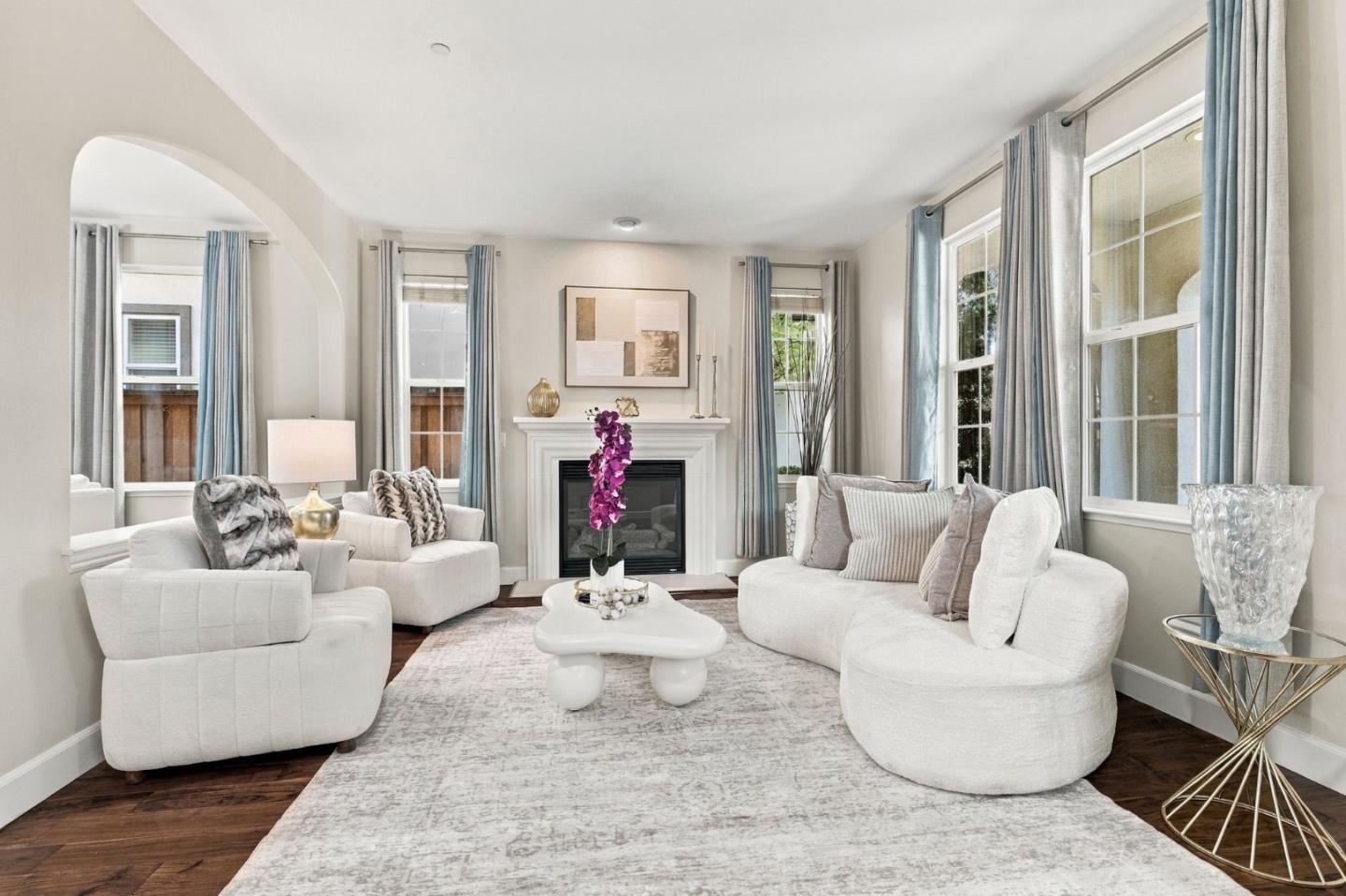Staged living room with white seating, a fireplace, blue-gray curtains, and dark wood floors.