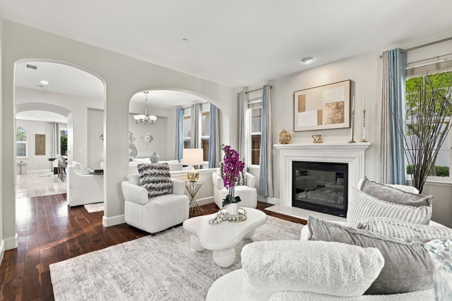 Staged living room with arched openings, white fireplace, and tall windows with blue curtains.