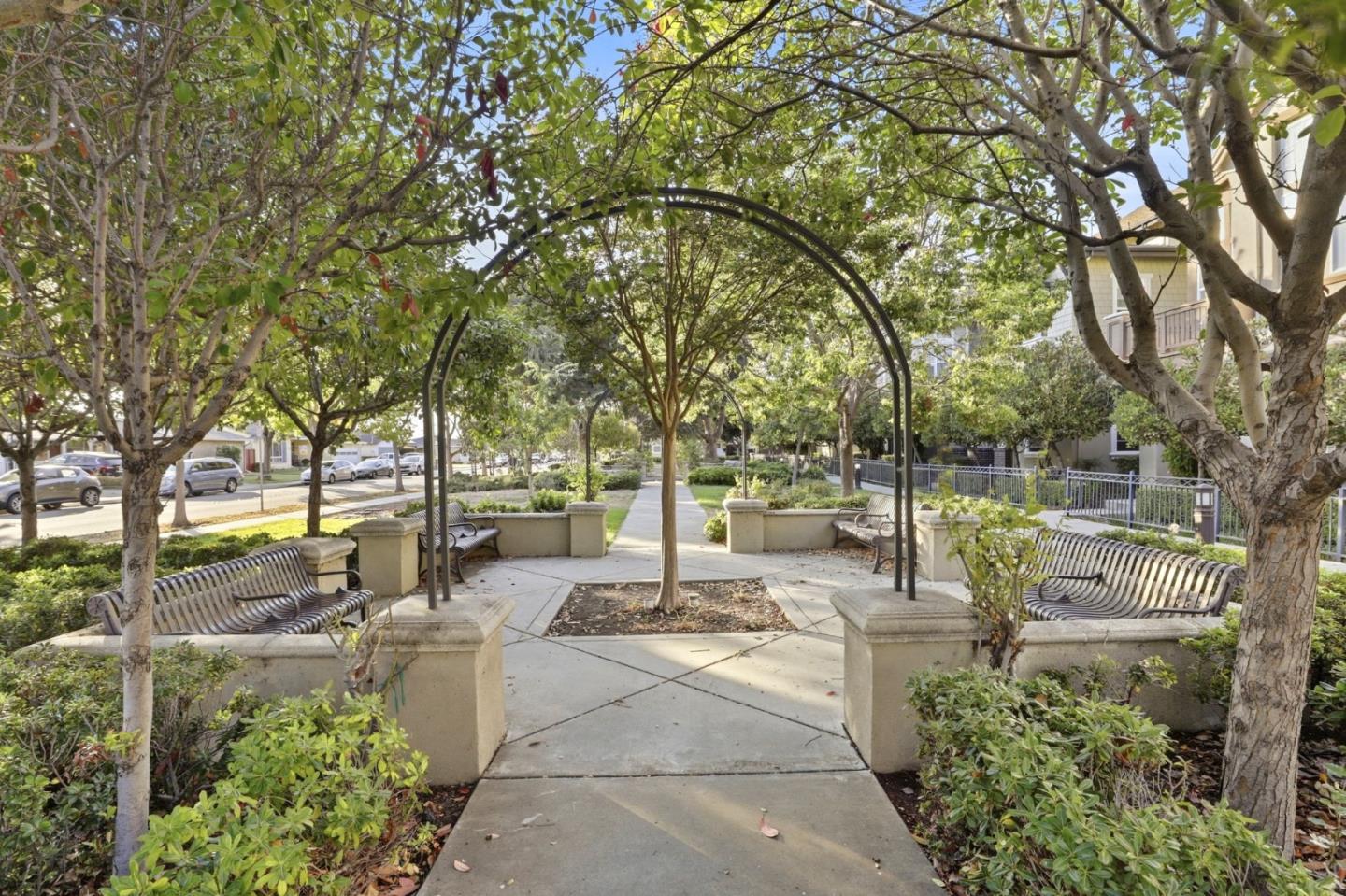 Landscaped courtyard with benches and a tree-covered arbor over a paved walkway.