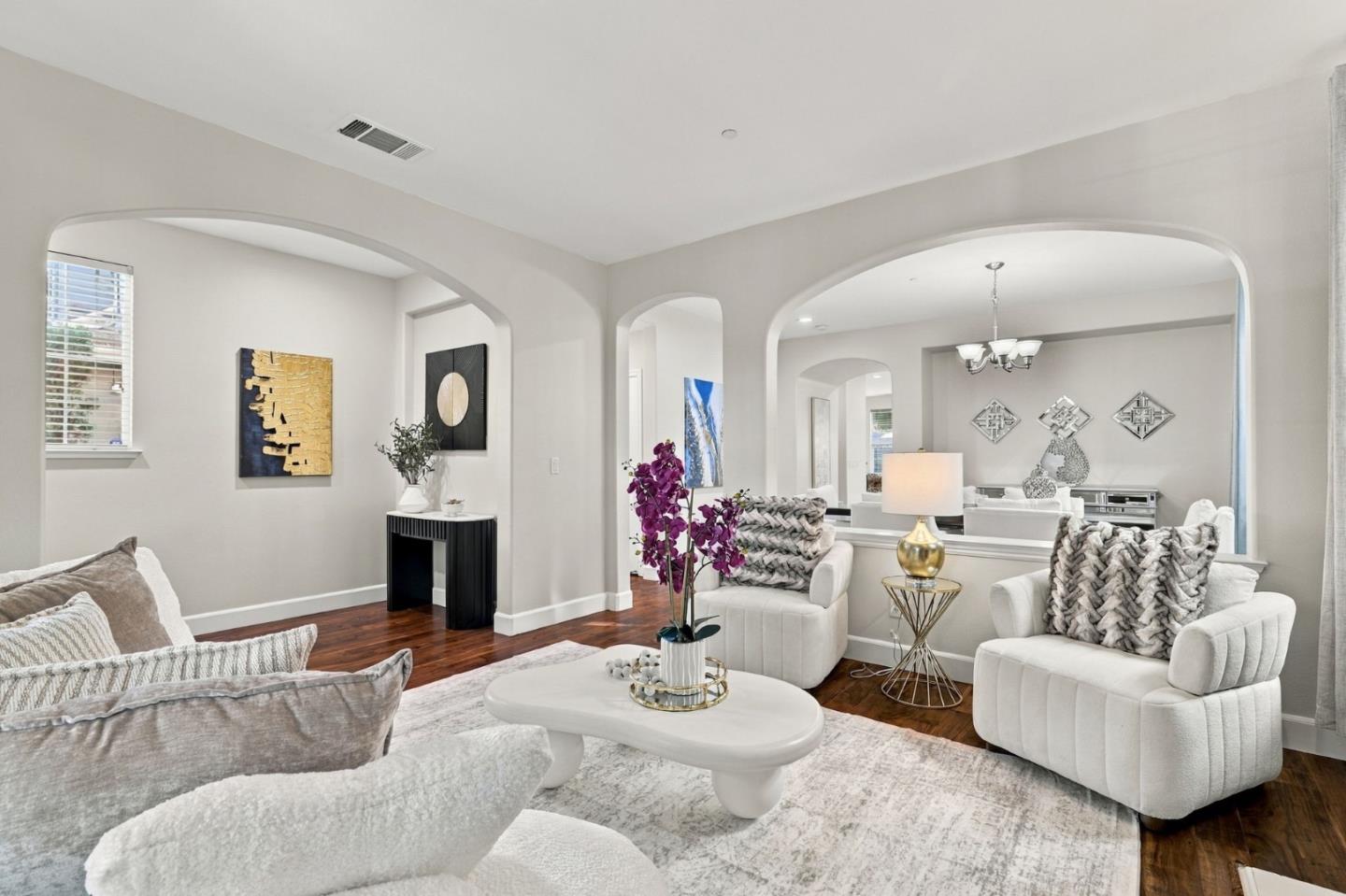 Staged living room with white seating, a sculptural coffee table, and wide arches opening toward the dining area.