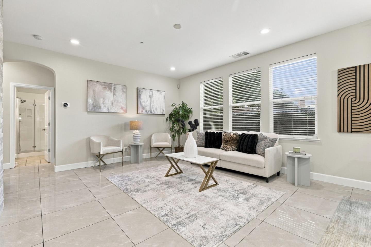 Staged living room with a white sofa, tiled floor, and large windows.