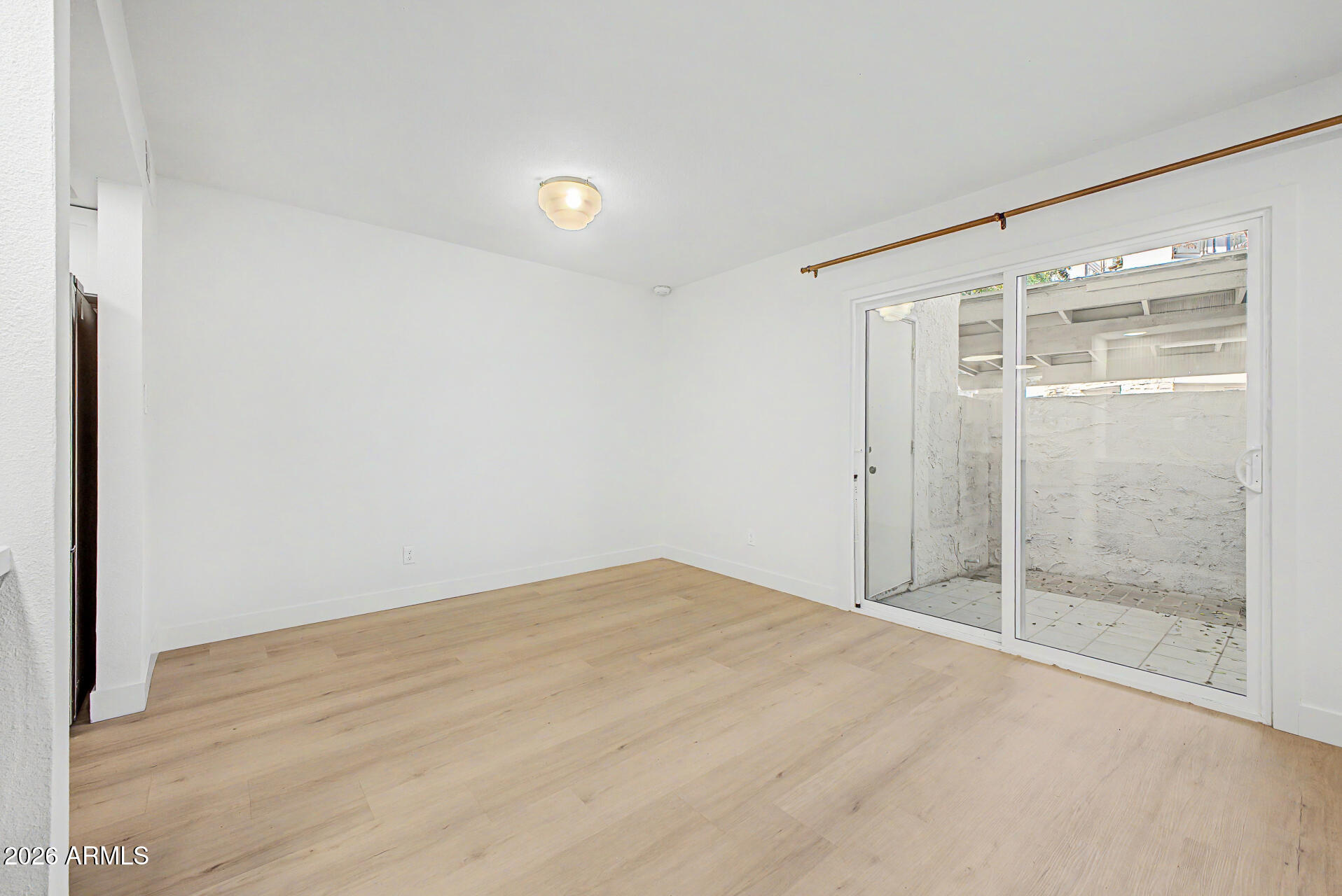 Empty room with light wood flooring and sliding glass doors opening to a tiled patio.