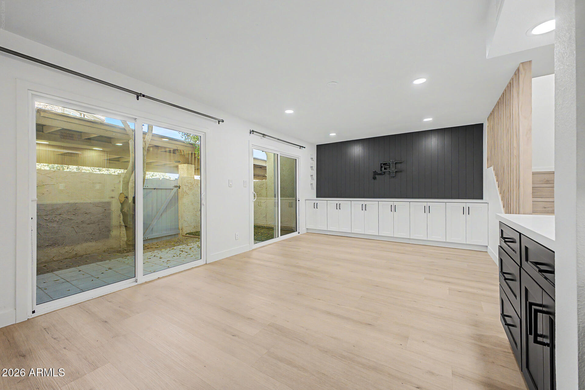Vacant living room with sliding patio doors, built-in cabinets, and a dark paneled media wall.