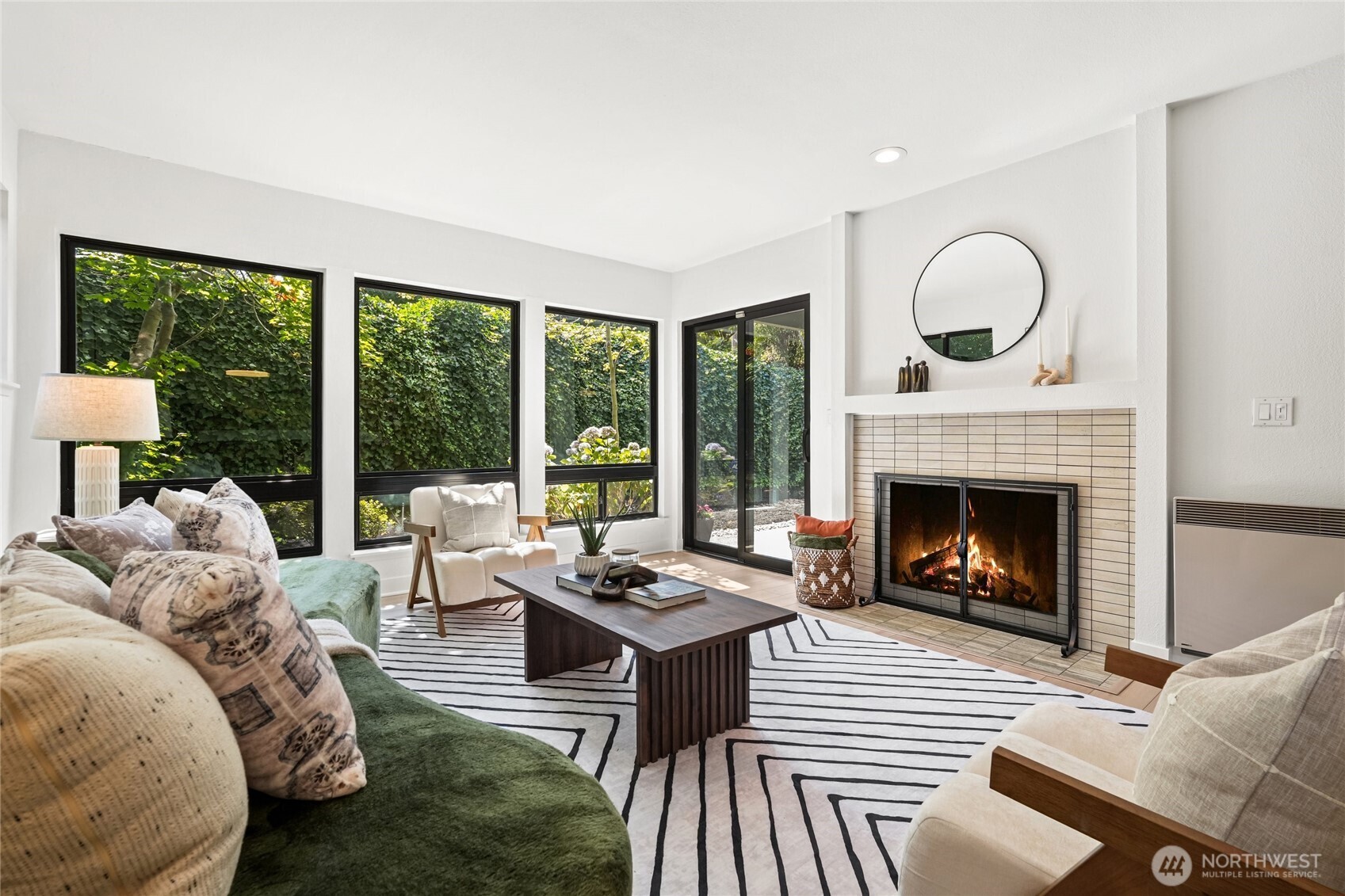 Living room with a tiled fireplace, large garden-facing windows, a green sofa, and cream armchairs.