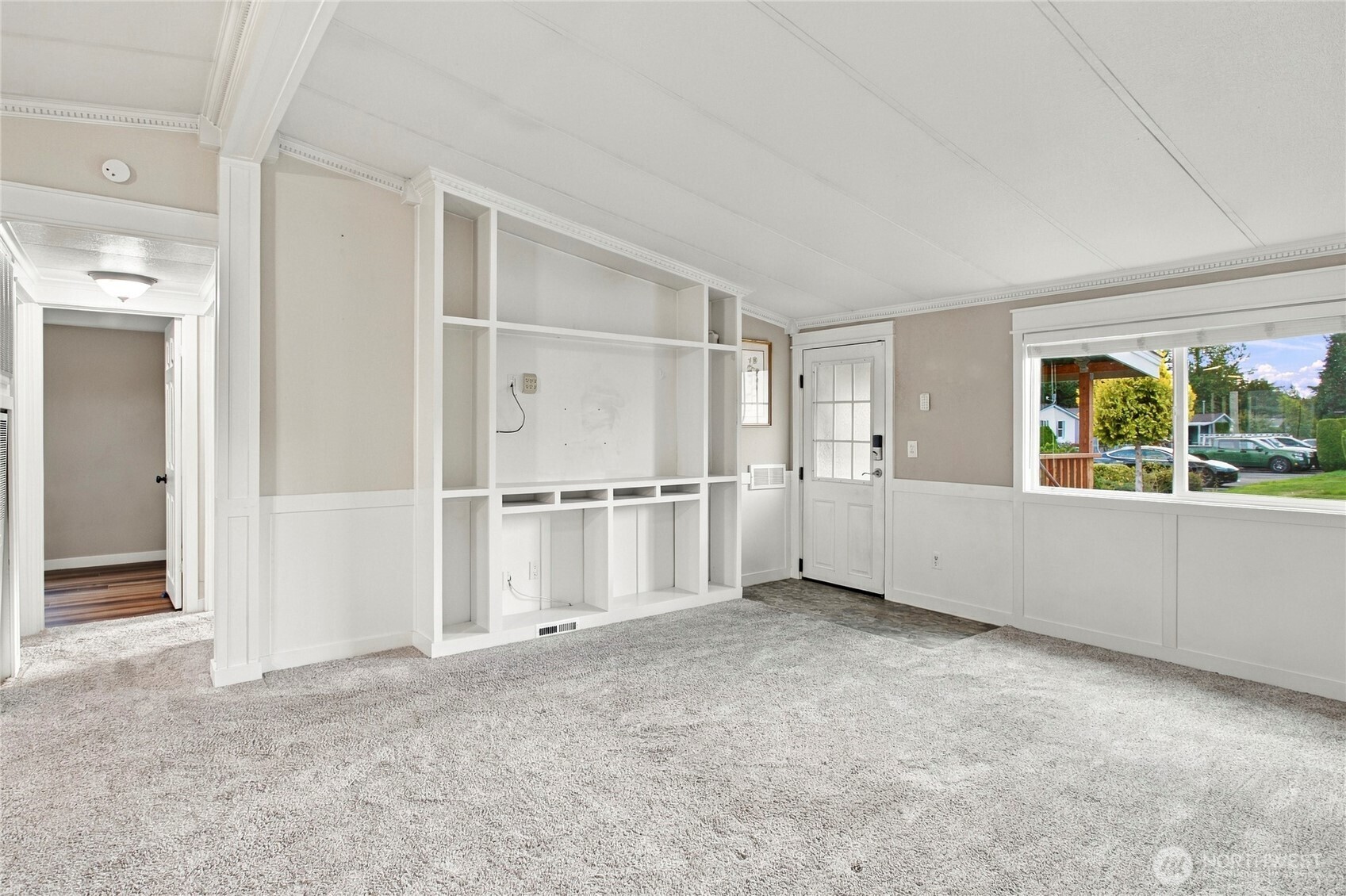 Empty living room with built-in white shelving, carpet, and a large window.