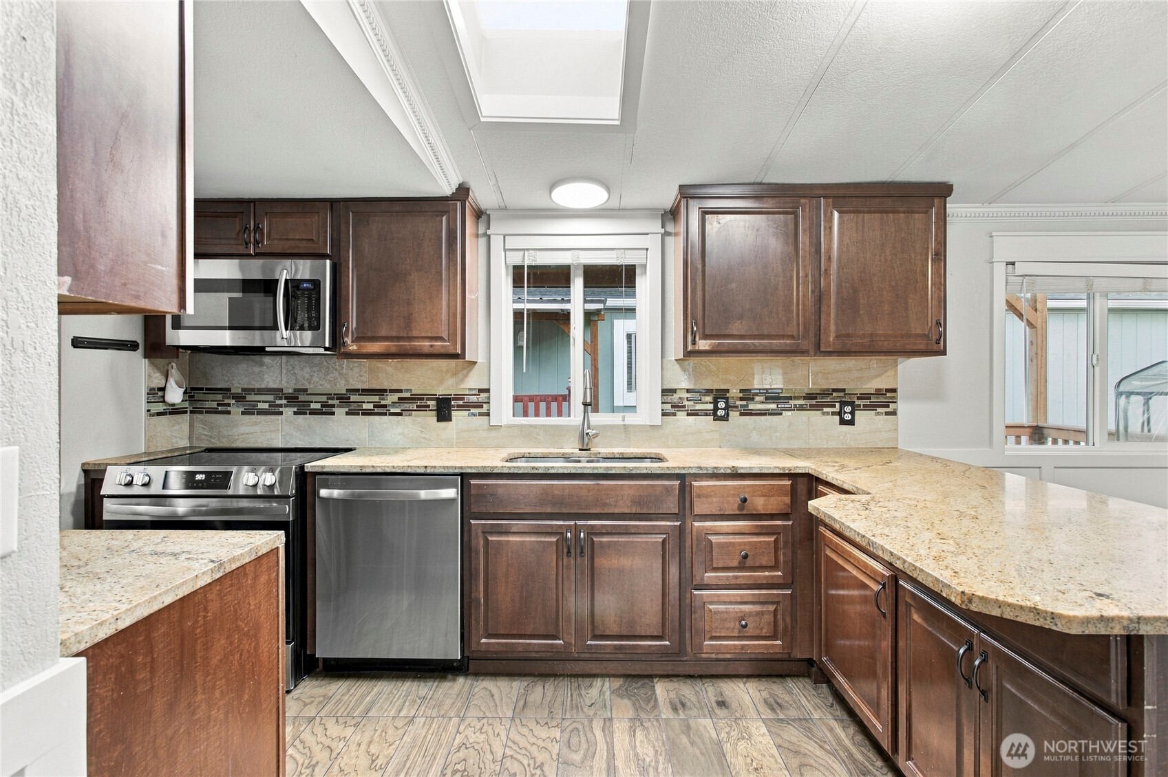 Kitchen with dark wood cabinets, granite counters, stainless steel appliances, and a window above the sink.