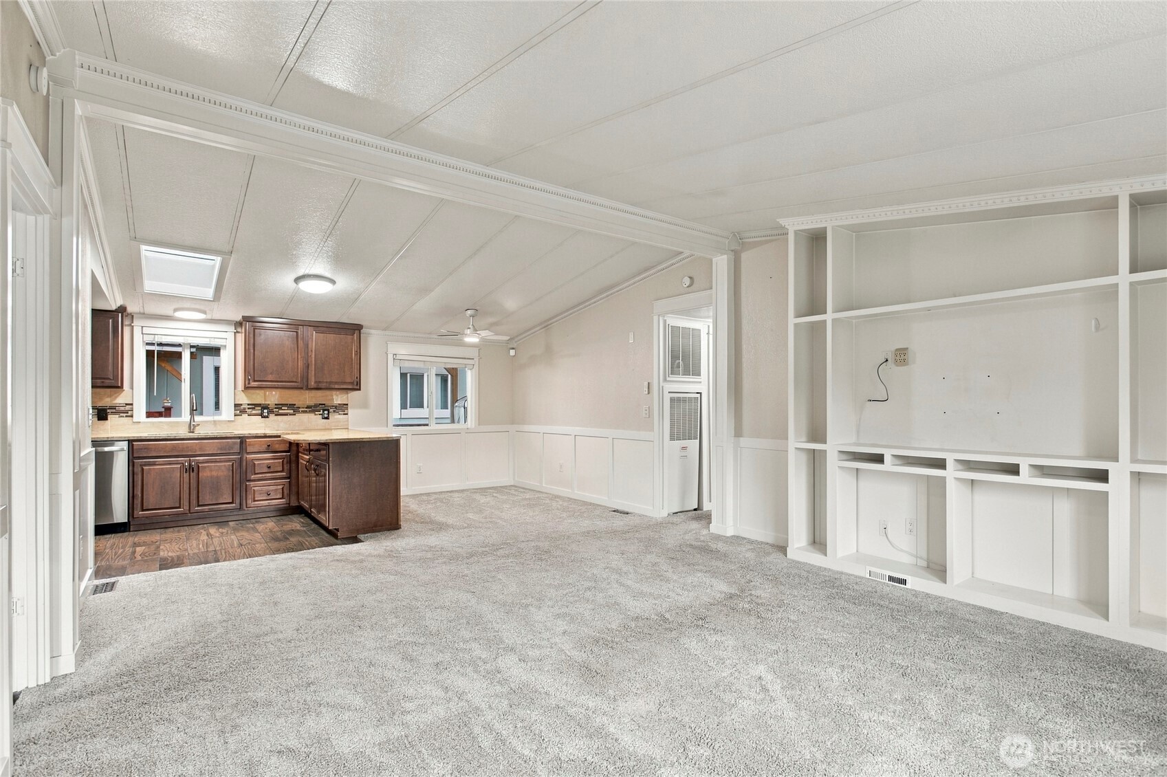Open living area with gray carpet, built-in shelving, and a dark wood kitchen.