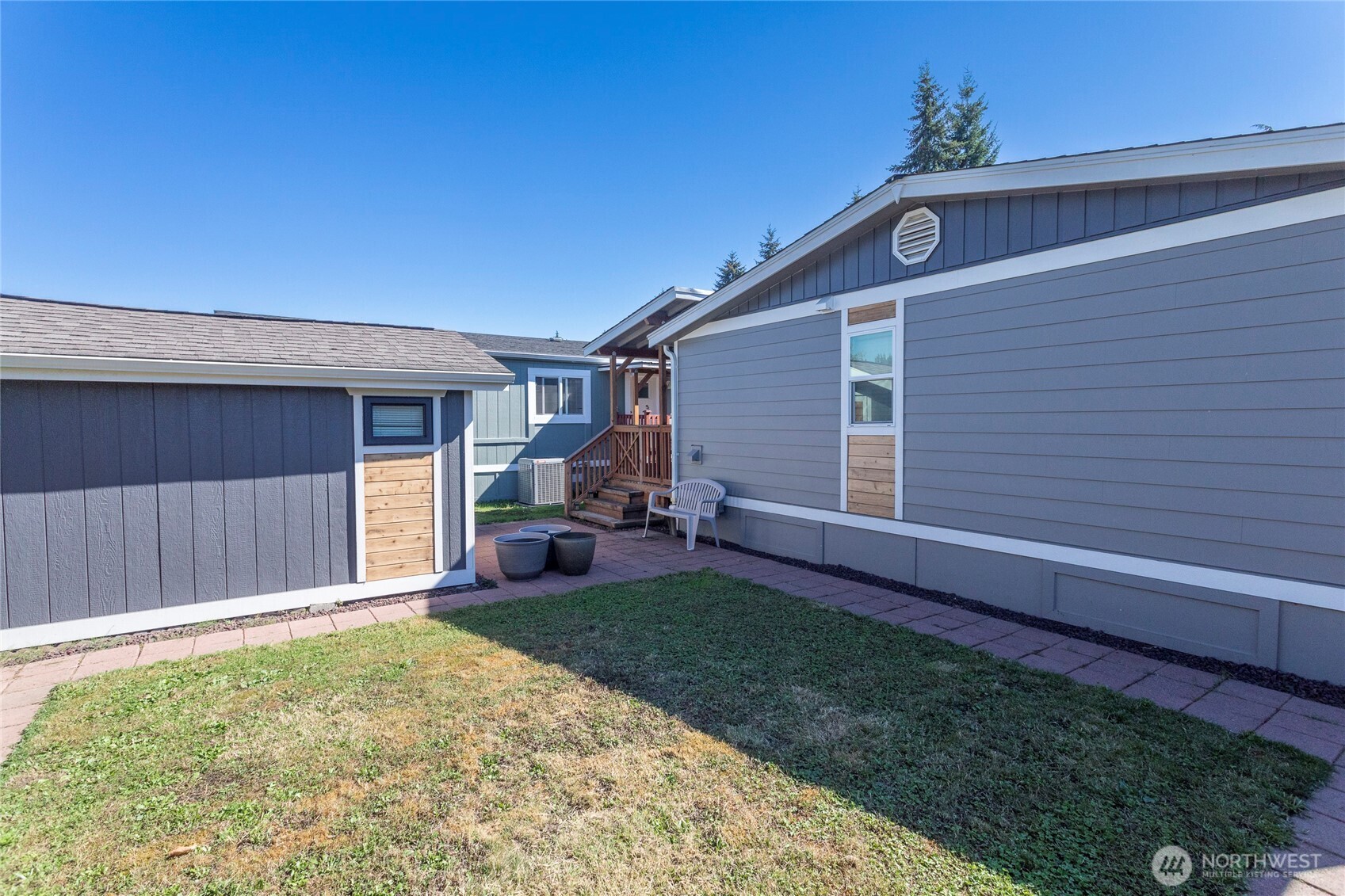 Home’s backyard courtyard with a paved path, lawn, patio chair, and detached shed.