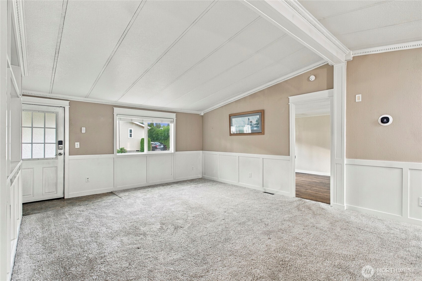 Empty living room with carpet, paneled walls, and an exterior entry door.