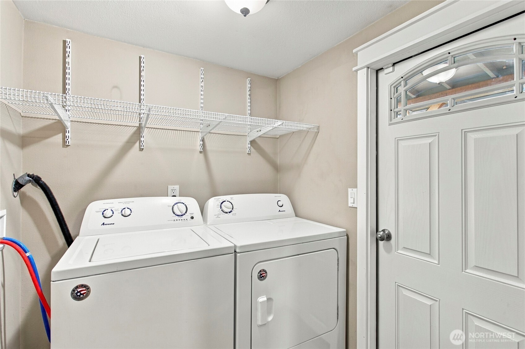 Laundry room with a white washer and dryer beneath wire shelving, beside a paneled door.