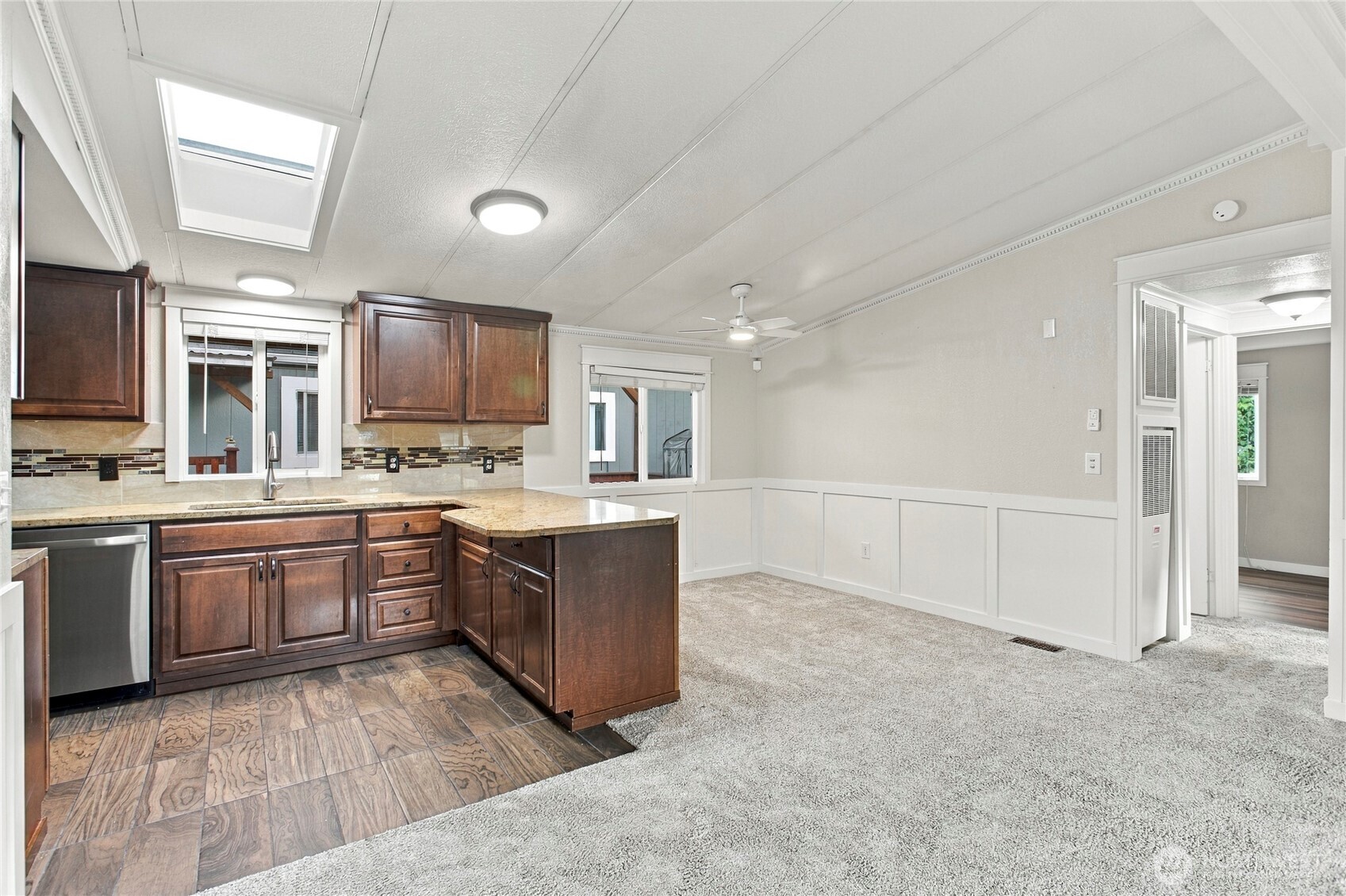 Kitchen with dark wood cabinets, a peninsula, skylight, and adjoining carpeted living area.