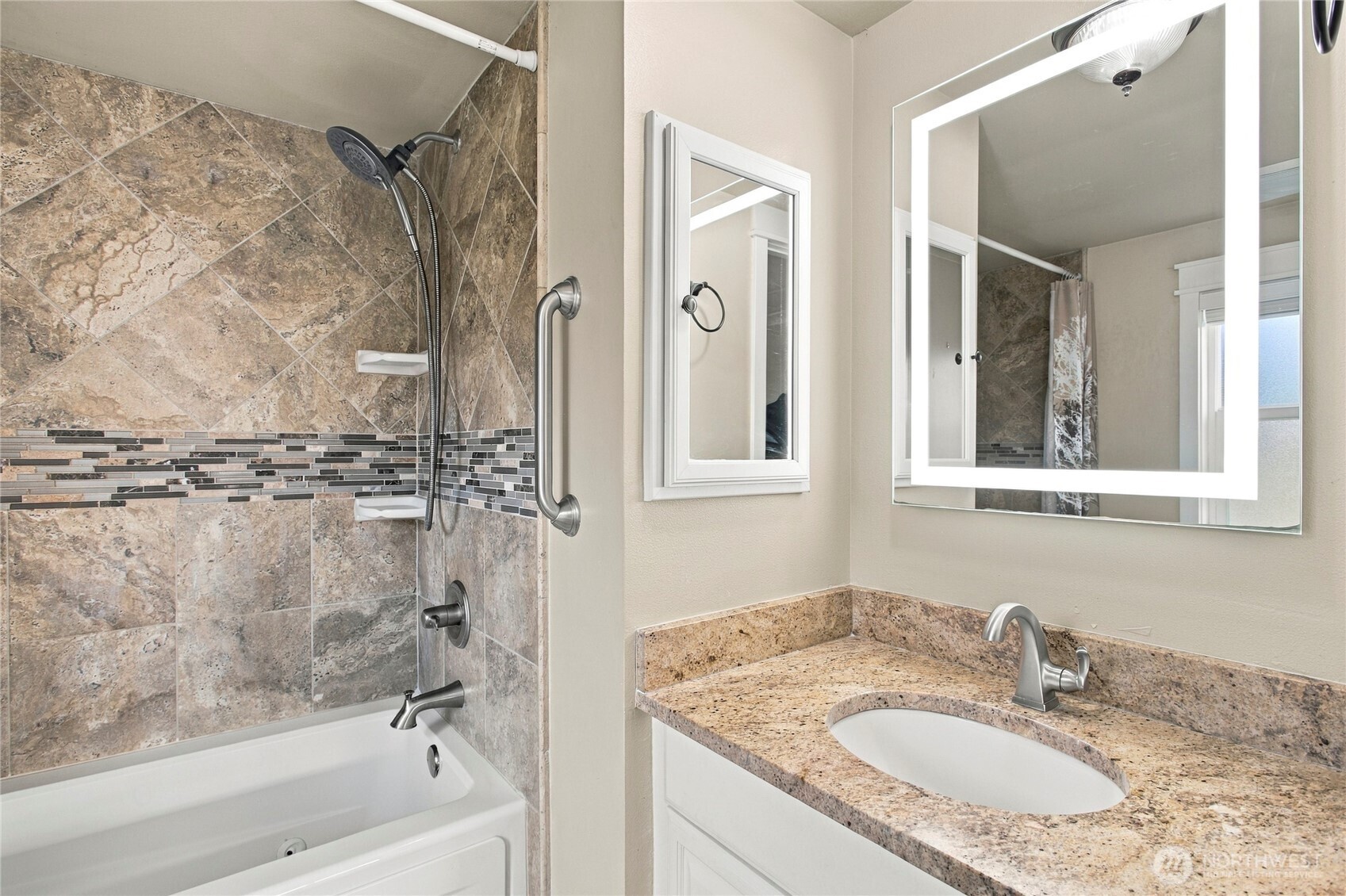 Bathroom with a tiled tub and shower beside a granite vanity and illuminated mirror.
