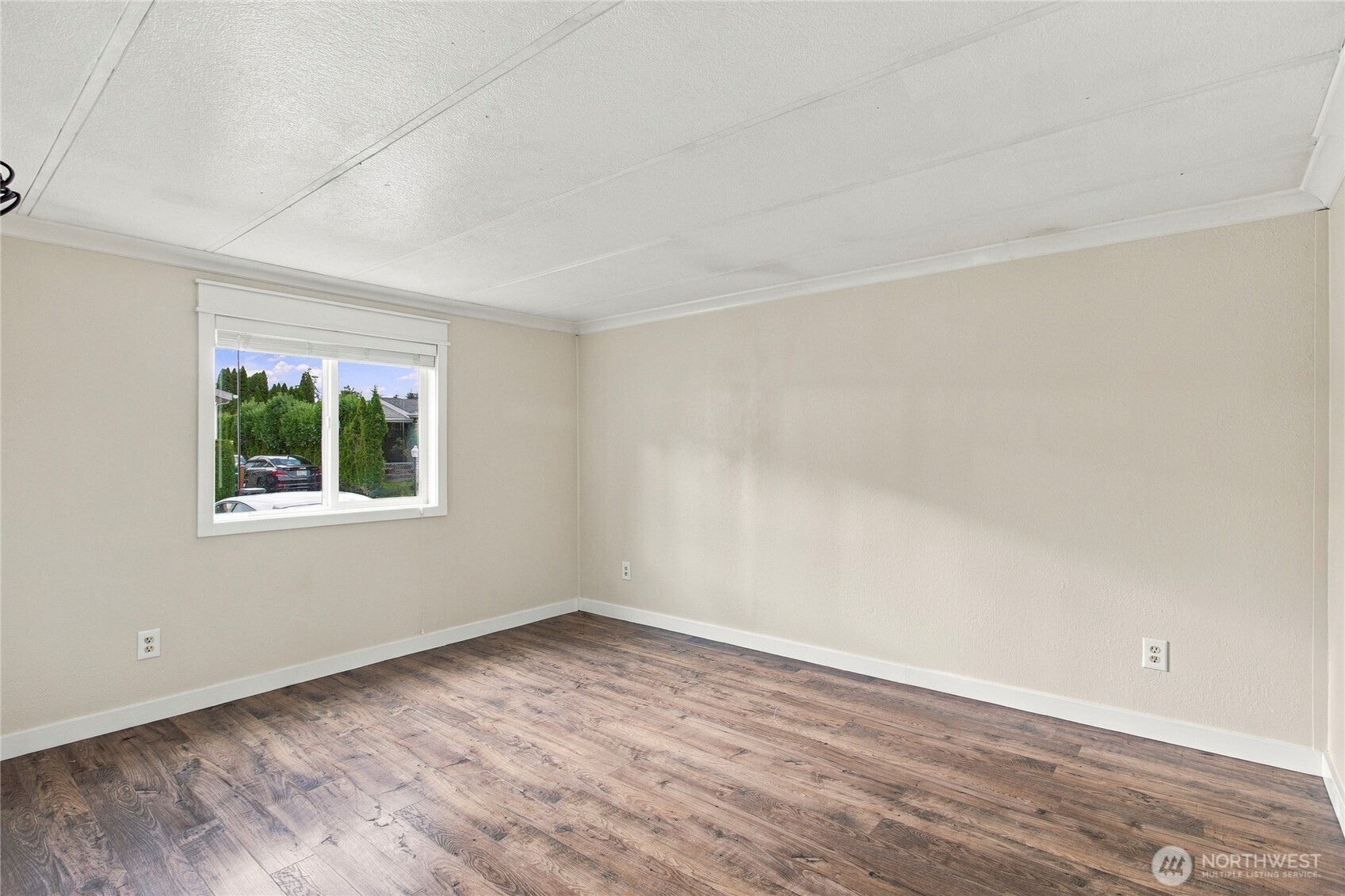 Empty room with wood-look flooring, beige walls, and a window overlooking greenery.