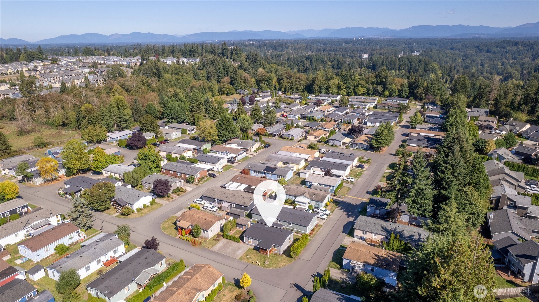 Aerial view of a residential neighborhood with a location marker and distant mountains.
