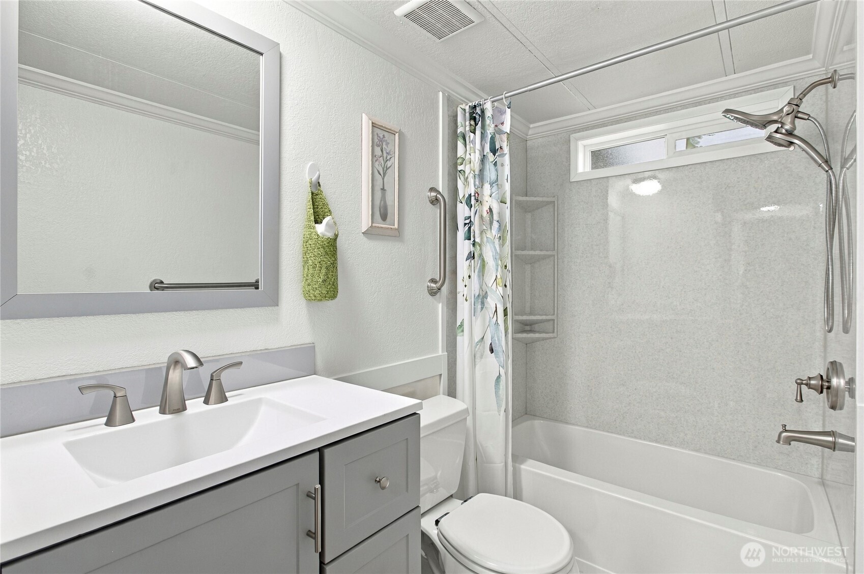 Bathroom with gray vanity, white tub and floral shower curtain.