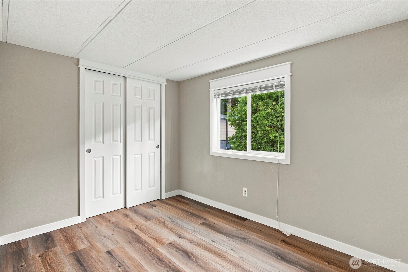 Empty room with wood-look flooring, white closet doors, and a window overlooking greenery.