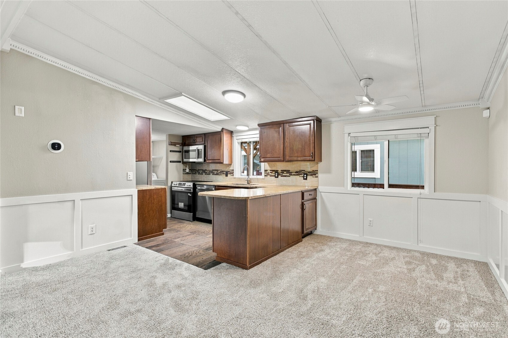 Living room with carpeted floor and an adjoining kitchen with a central island and dark wood cabinets.