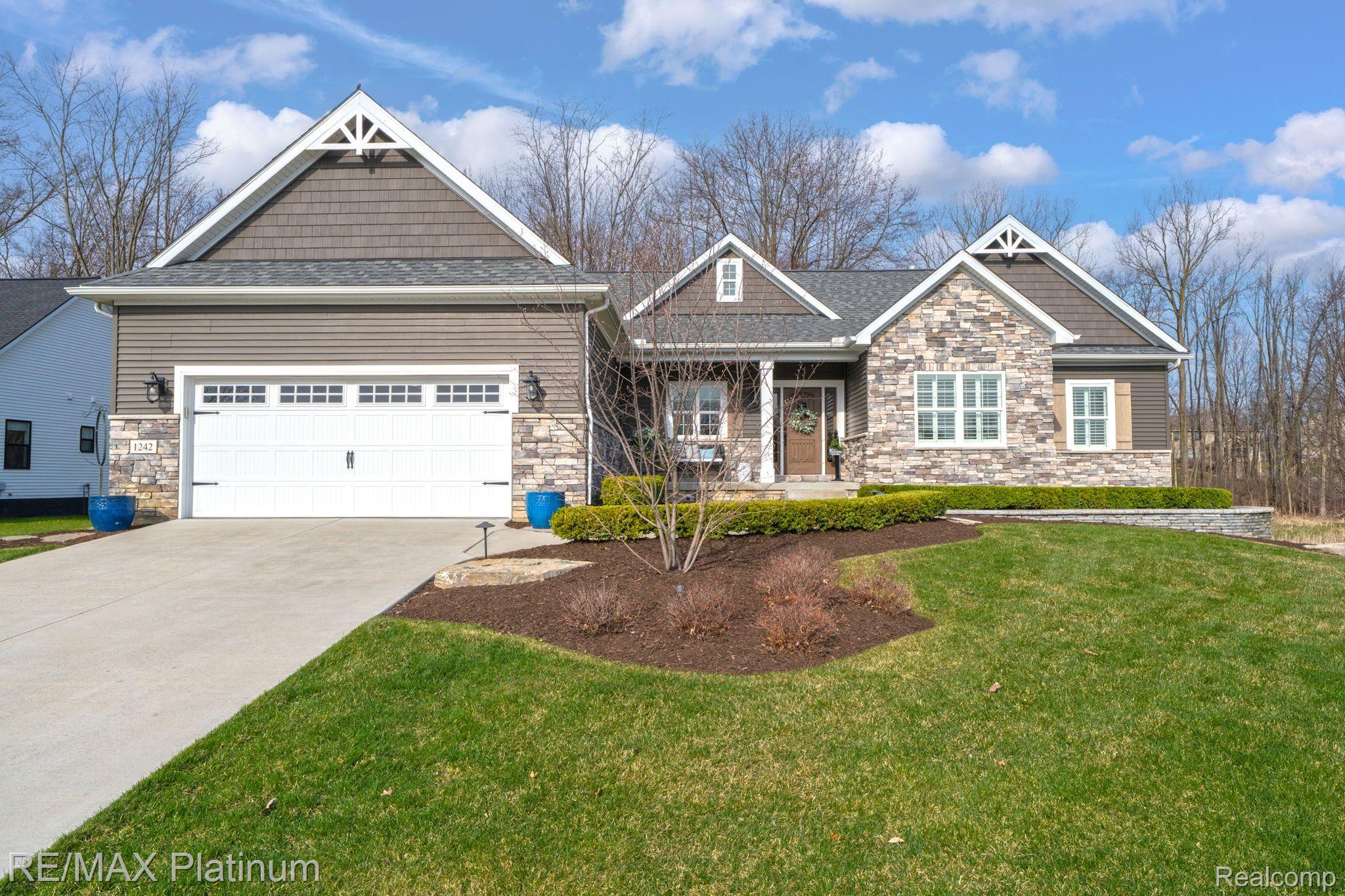 Gray-brown home with stone facade, multiple gables, white garage, and landscaped front lawn.