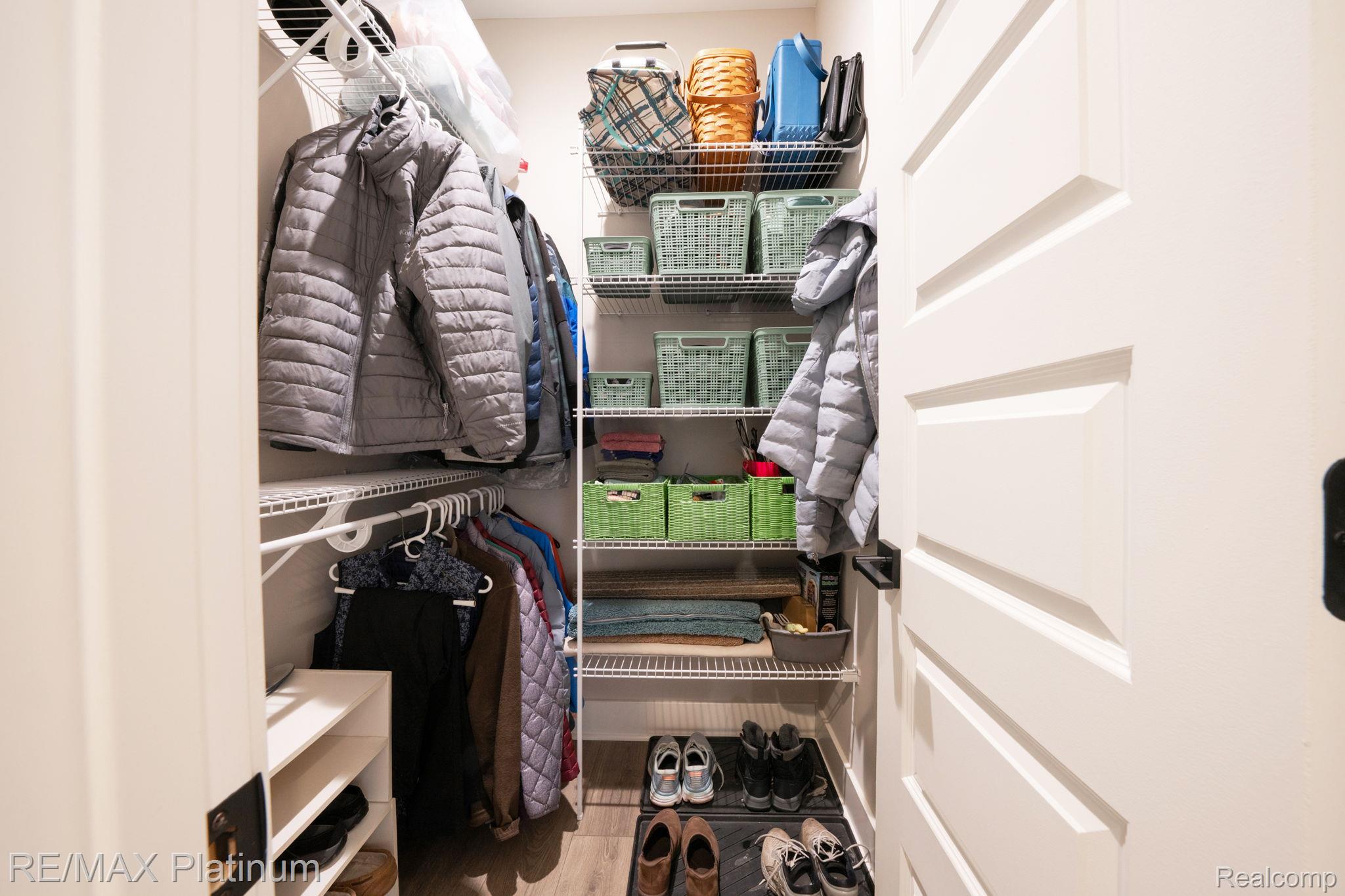 Walk-in closet with organized shelves, green baskets, hanging coats, folded linens, and shoes.