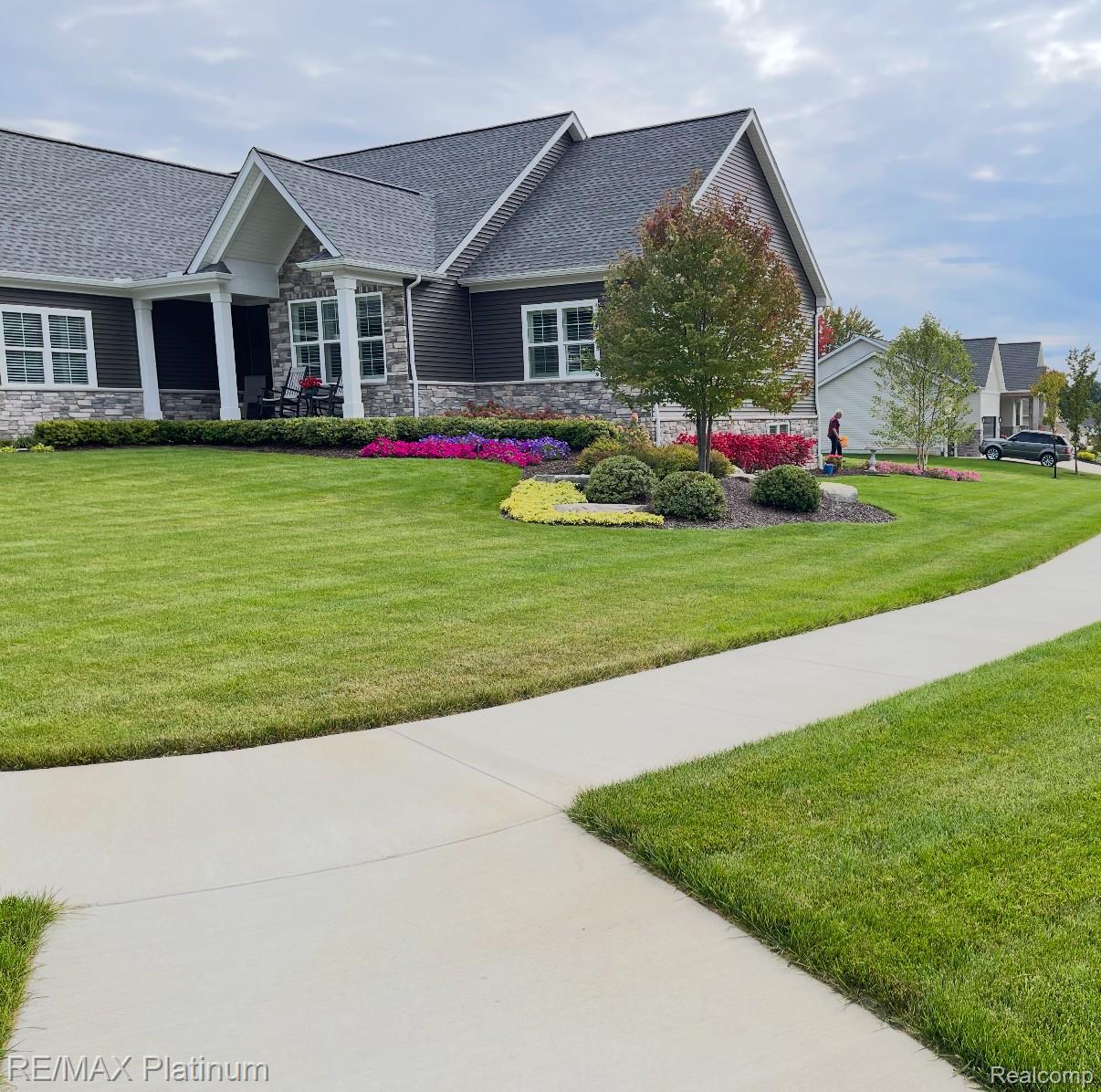 Home exterior with stone accents, a covered porch, colorful flower beds, and a curving sidewalk.