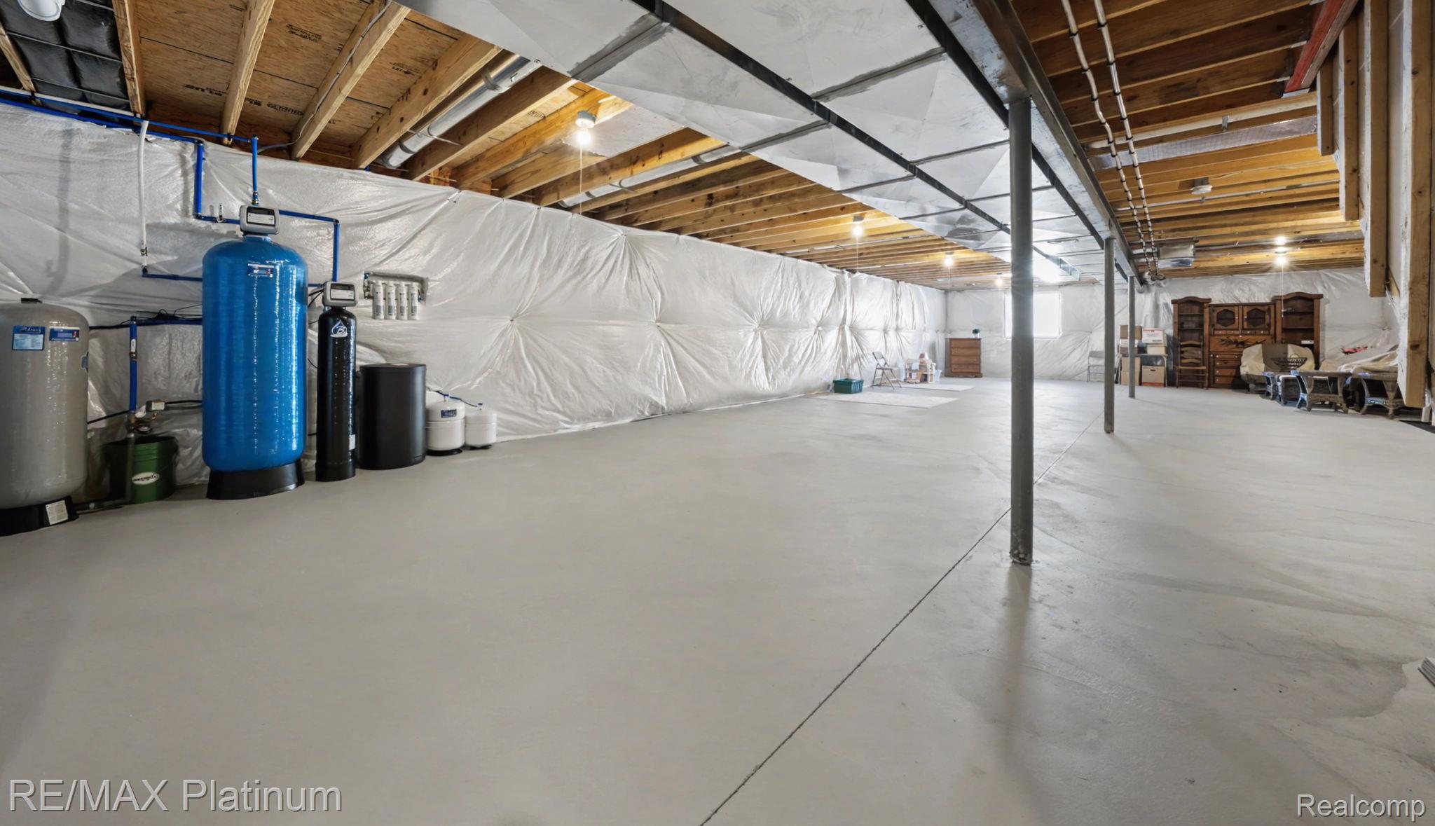 Unfinished basement with a broad concrete floor, exposed joists, ductwork, and water treatment equipment.