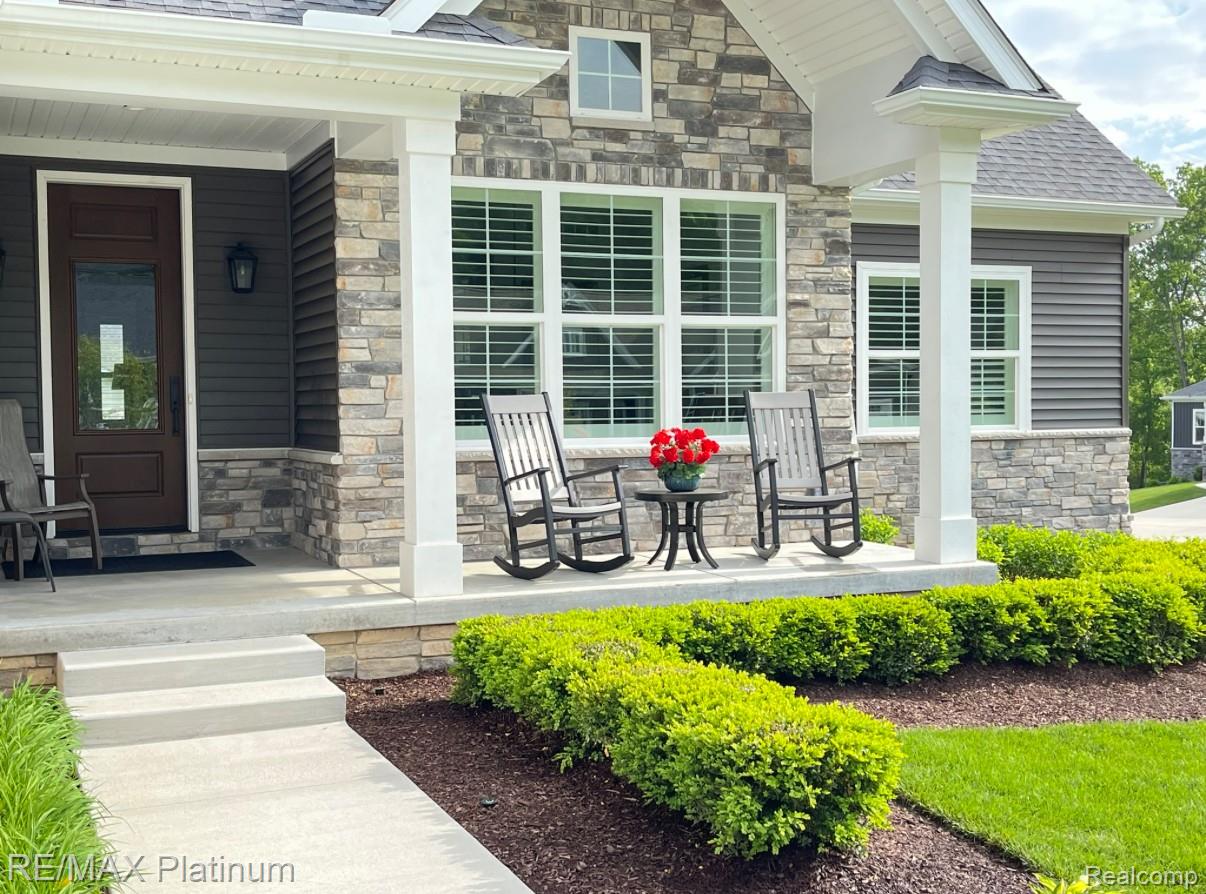 House front with a stone facade, covered porch, rocking chairs, and landscaped shrubs.
