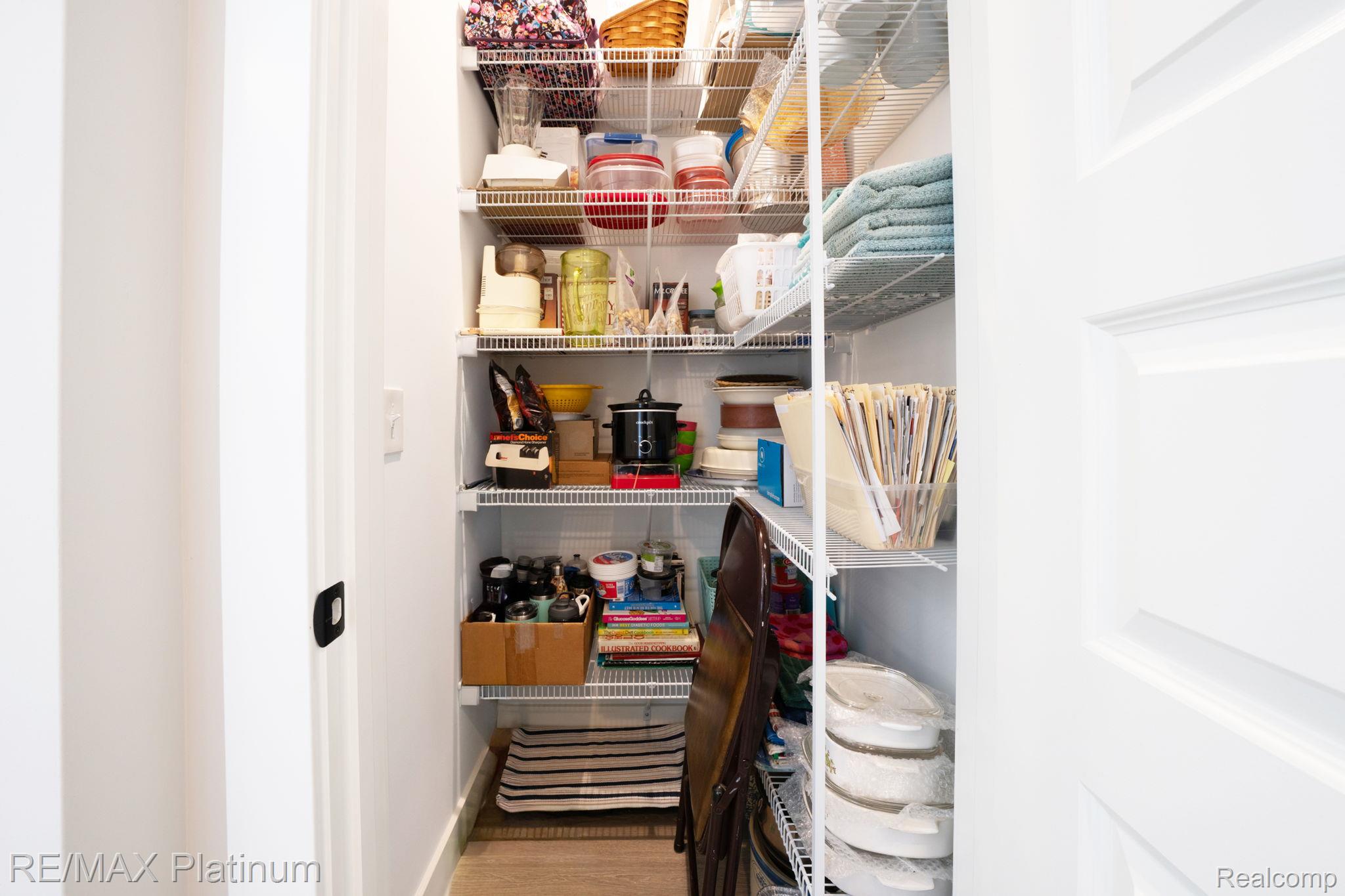 Walk-in pantry with white wire shelving stocked with containers, towels, cookware, and household supplies.