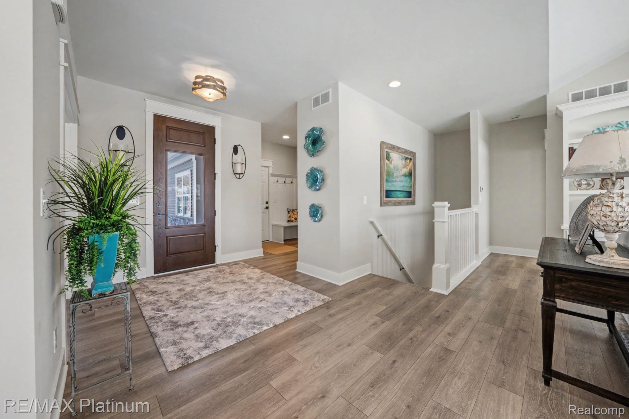 Entry foyer with a glass-paneled wood door, plank flooring, patterned rug, and staircase.