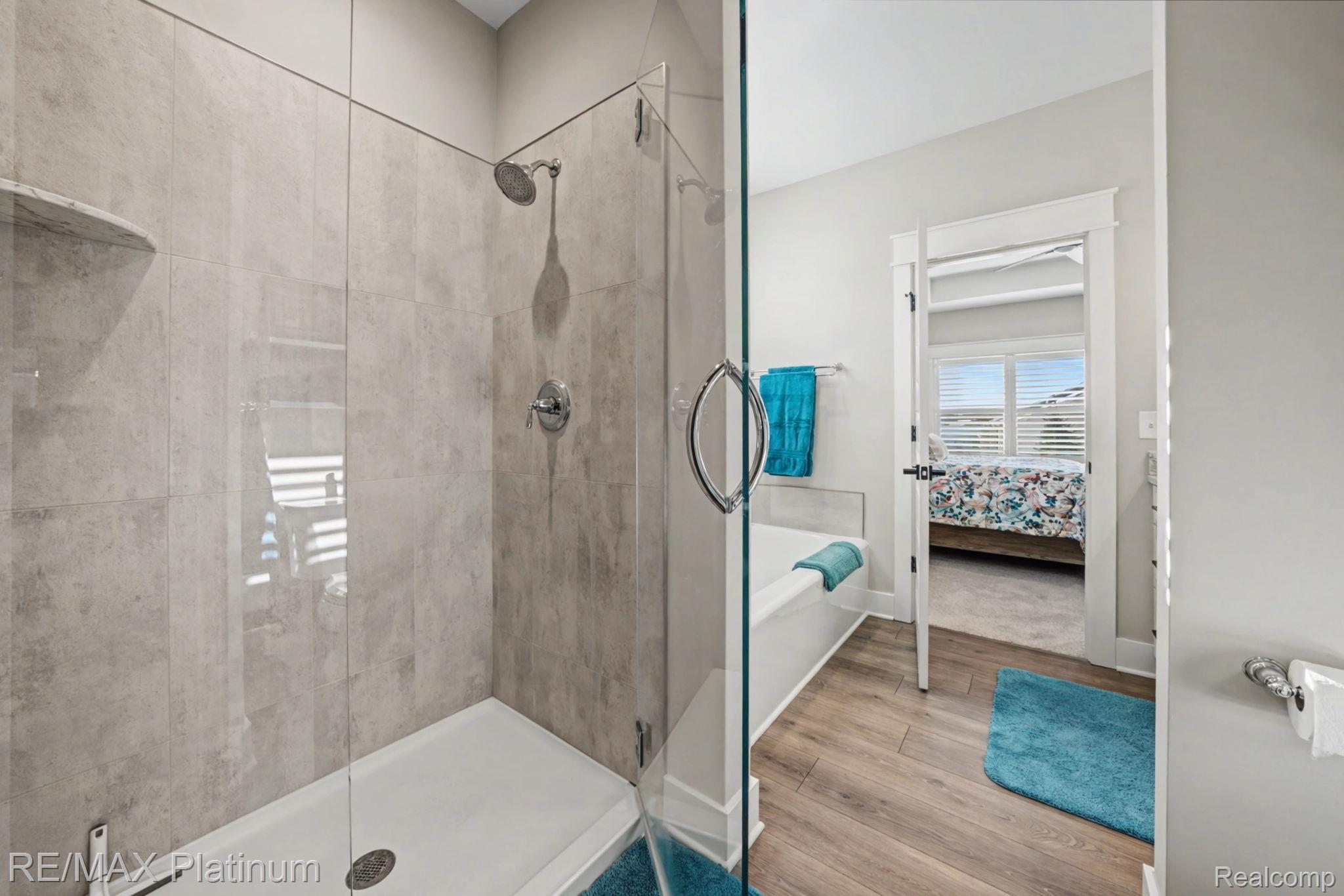 Bathroom with a glass-enclosed gray-tile shower, white tub, turquoise towels, and wood-look flooring.