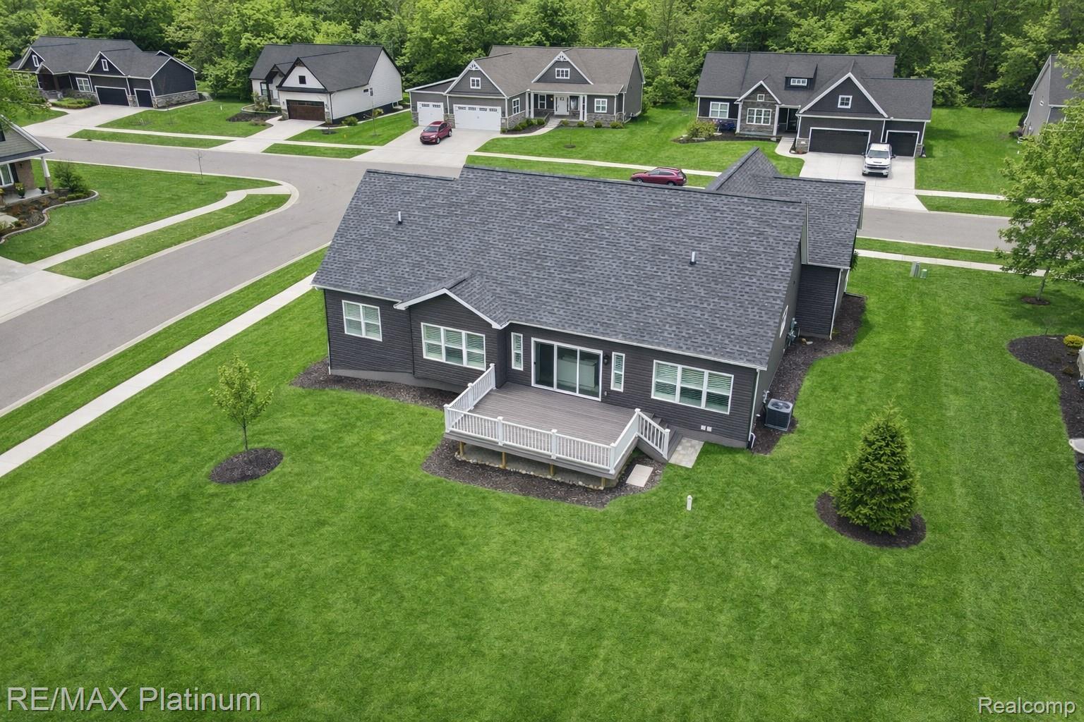 Aerial view of a dark gray home with a raised white-railed deck and broad lawn.