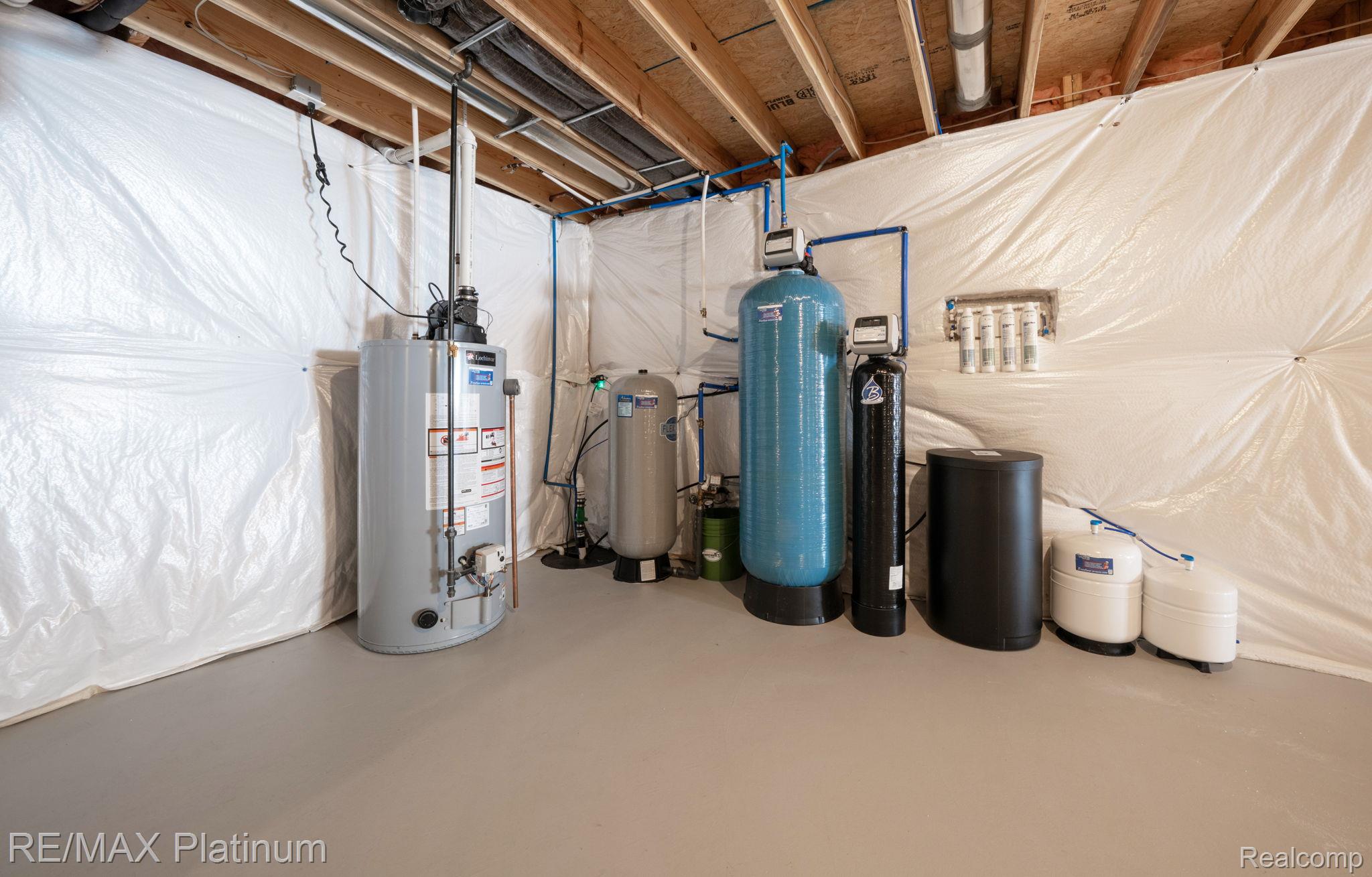 Basement utility room with a water heater and water filtration equipment beneath exposed ceiling joists.
