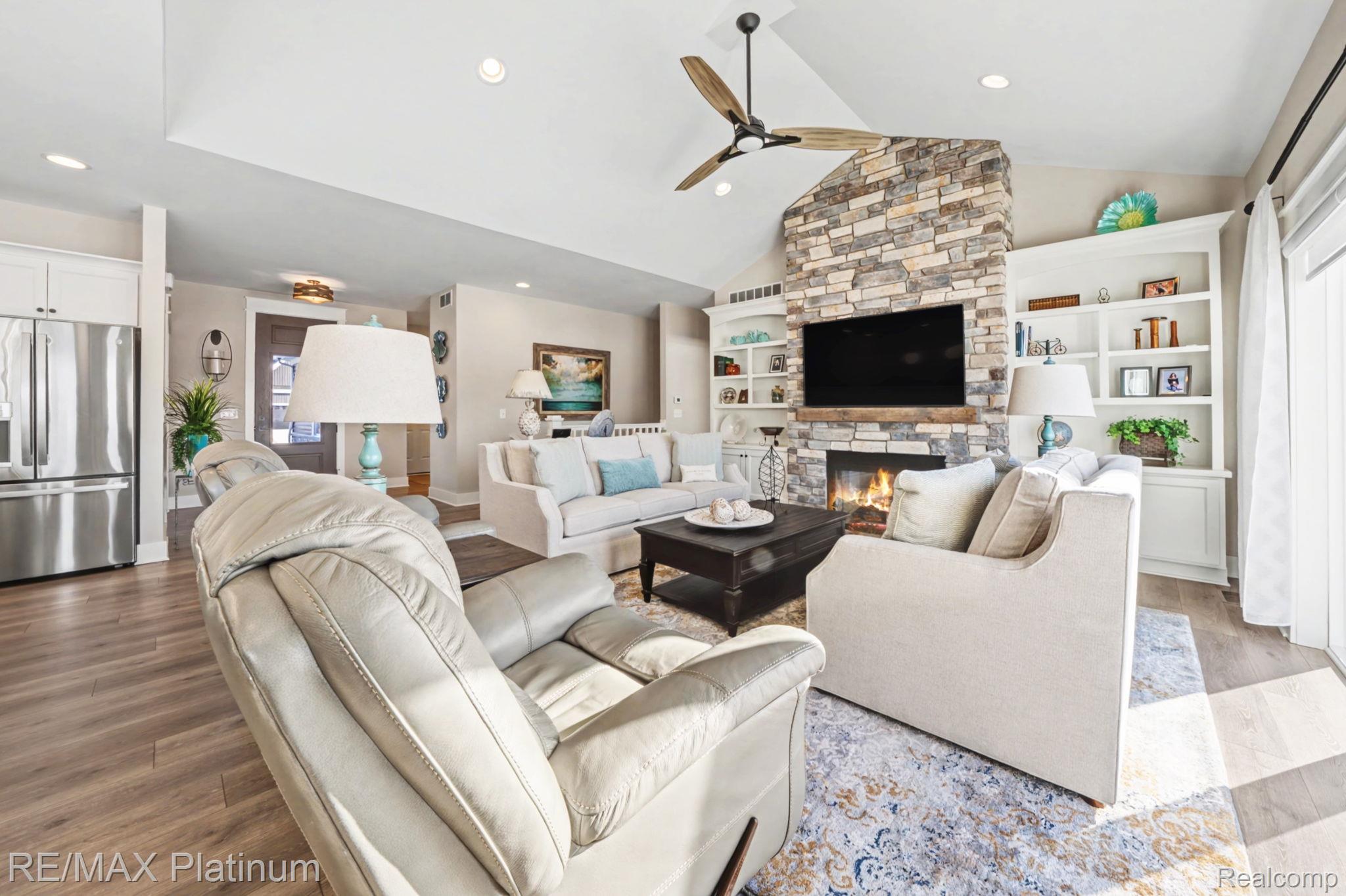 Living room with vaulted ceiling, stone fireplace, built-in shelving, and a view of the kitchen.