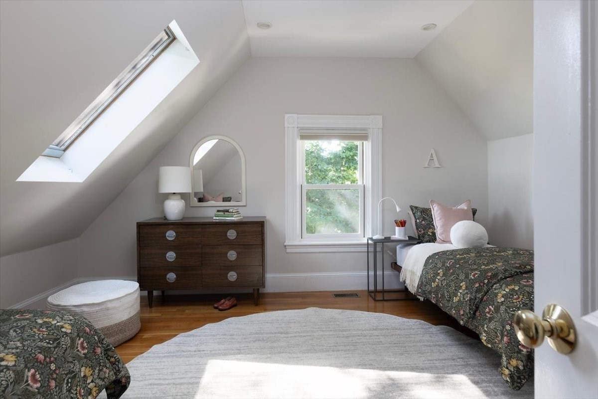 Attic bedroom with a large skylight, sloped ceilings, hardwood floors, and floral bedding.