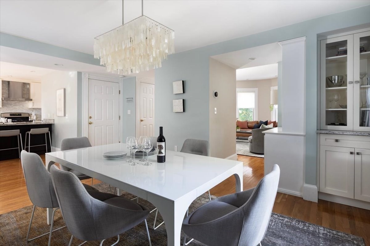 Dining room with a white table, gray chairs, and a sculptural chandelier beside the open kitchen.