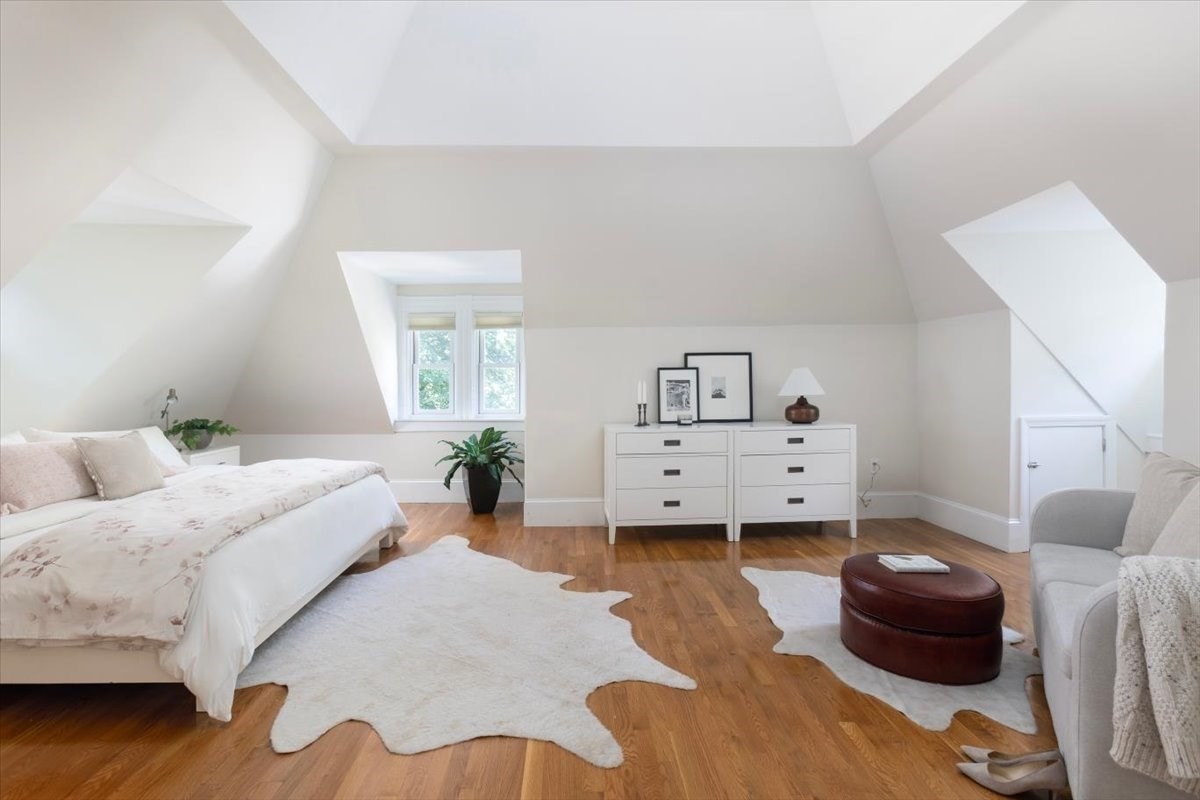 Attic bedroom with a sloped ceiling, dormer window, white furnishings, and warm wood floors.