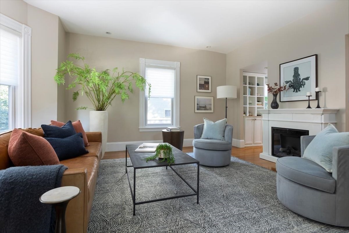 Staged living room with a white fireplace, tan sofa, pale blue armchairs, and large windows.